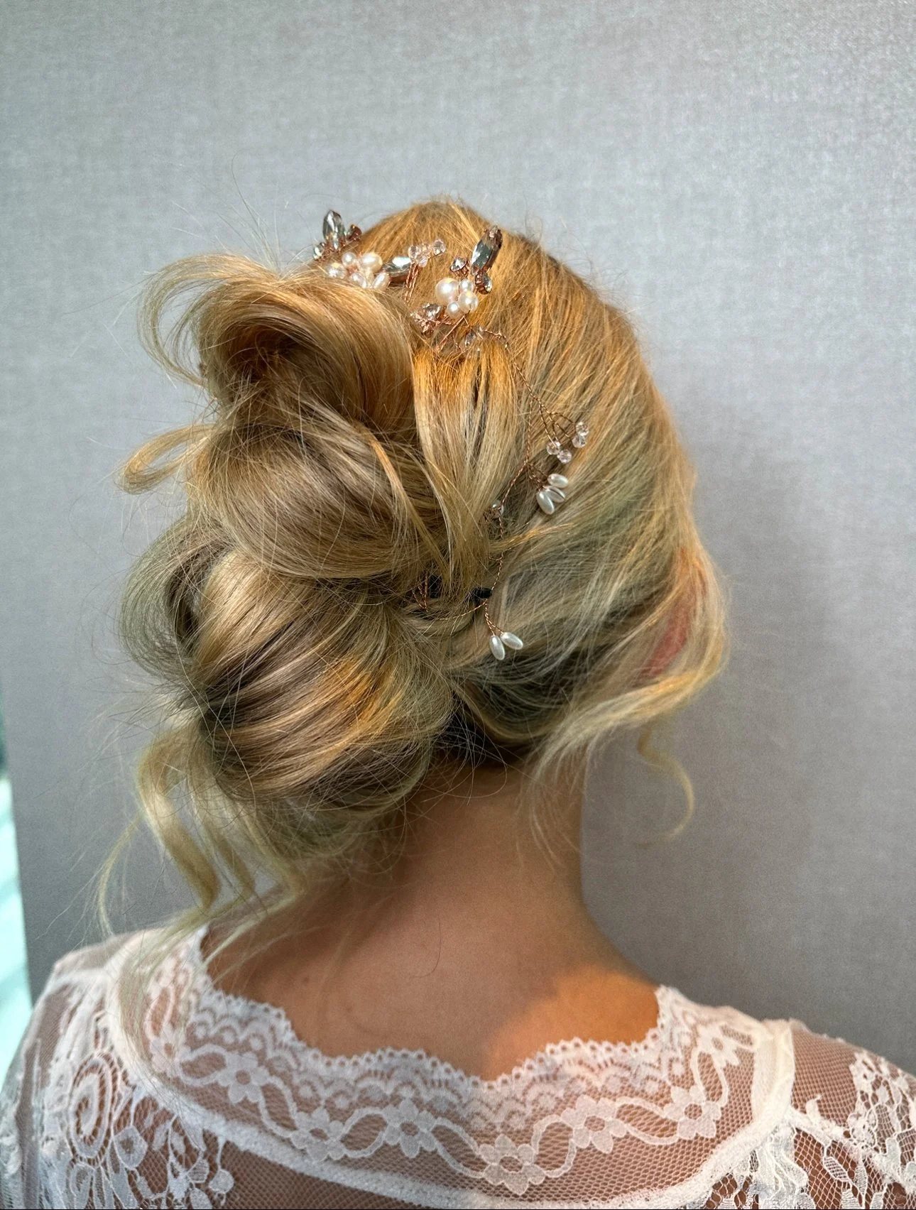 A woman with blonde hair styled in an elegant updo, decorated with pearl and crystal hair accessories, wearing a lace garment