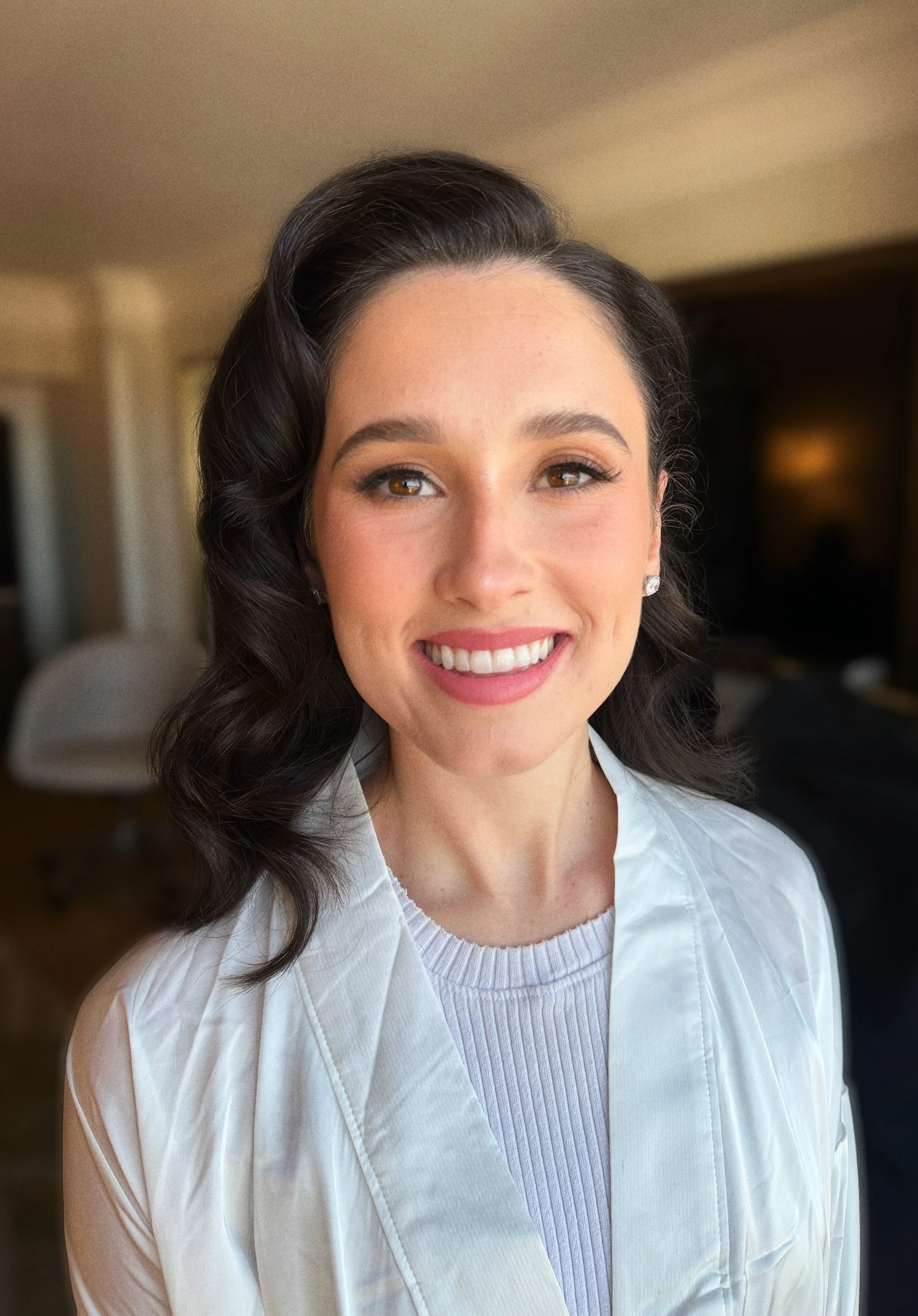 A woman with dark, wavy hair and light skin smiling in a well-lit room.