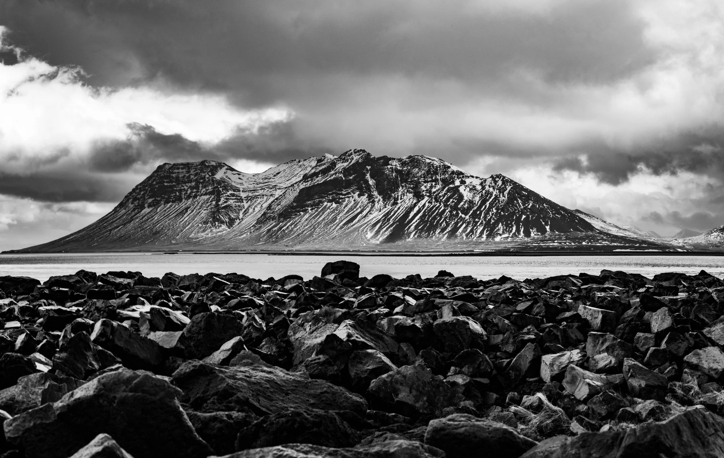 Black and white fine art landscape of dramatic Icelandic mountain and rocky shoreline, captured roadside in Iceland