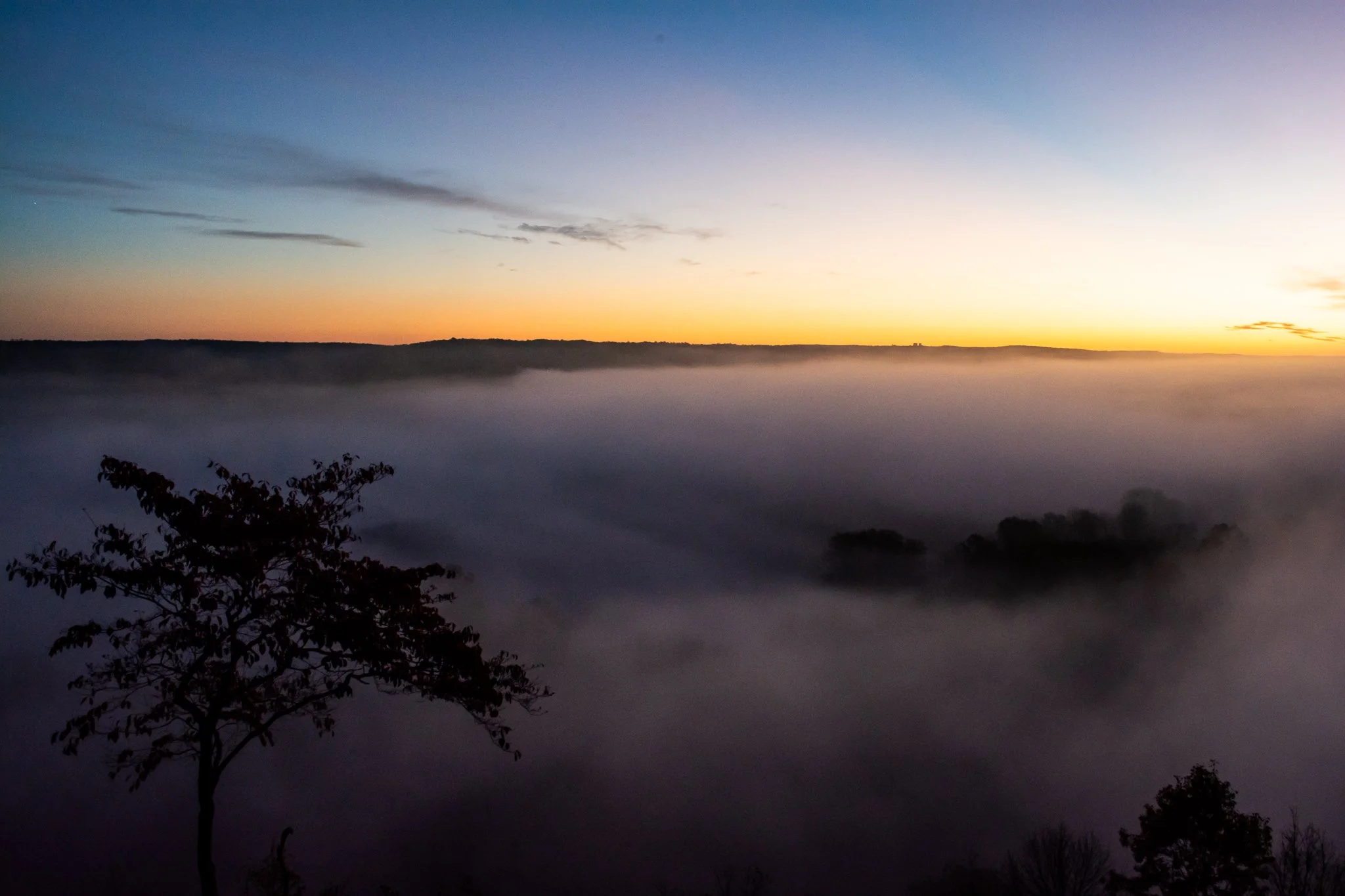 Sunrise over fog-filled valley at War Eagle Mill, Rogers Arkansas – golden orange sky and layered mist landscape