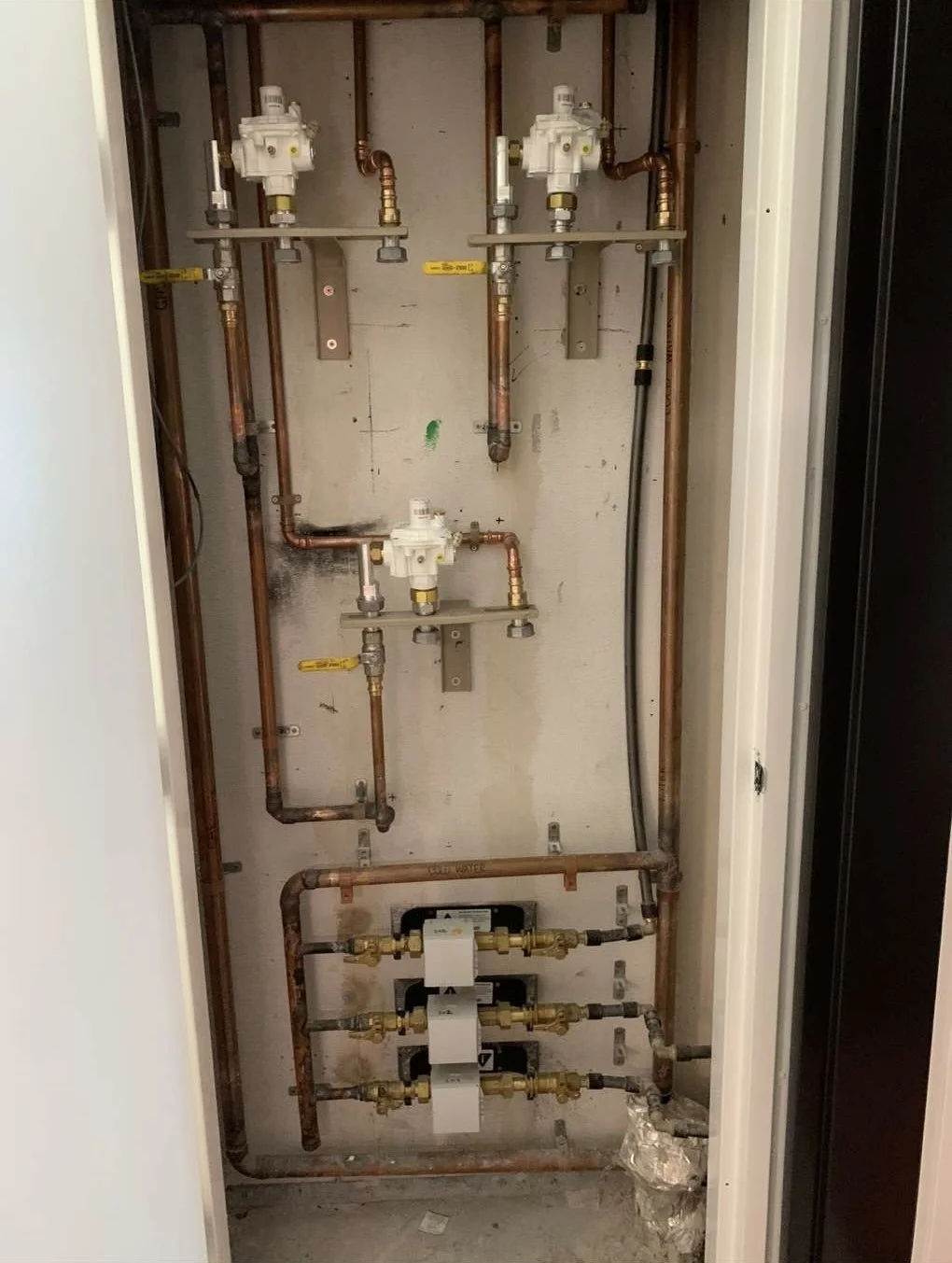Plumbing pipes and valves inside a wall cabinet, including copper pipes and white valves.