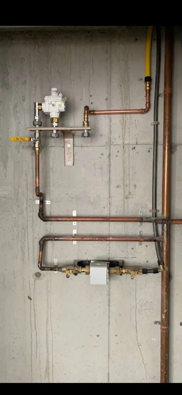A plumbing setup with copper pipes, a water meter, and various valves mounted on a concrete wall.