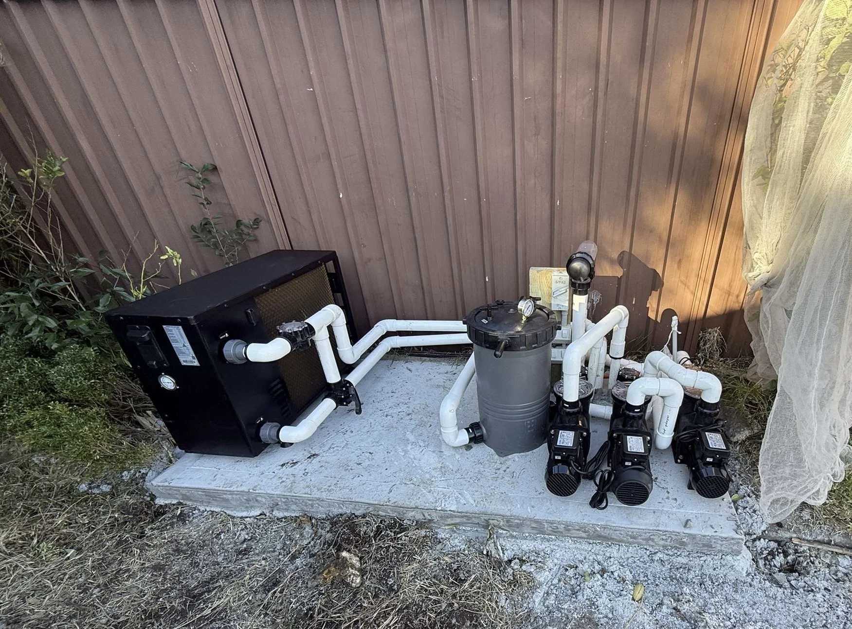 Outdoor pool pump and filtration system with white PVC pipes on a concrete slab