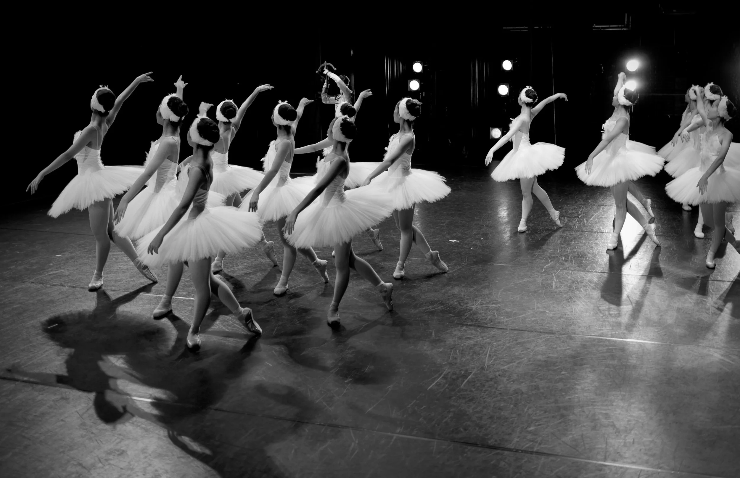 Ballet dancers in white tutus practicing on a stage with lighting effects.