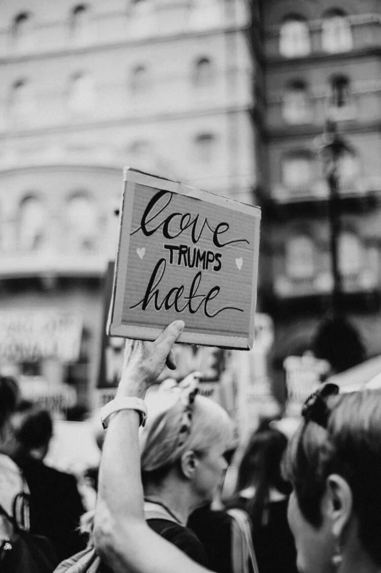 Black and white photo of a protest with a sign reading 'love trumps hate' held aloft by a participant in a crowd.