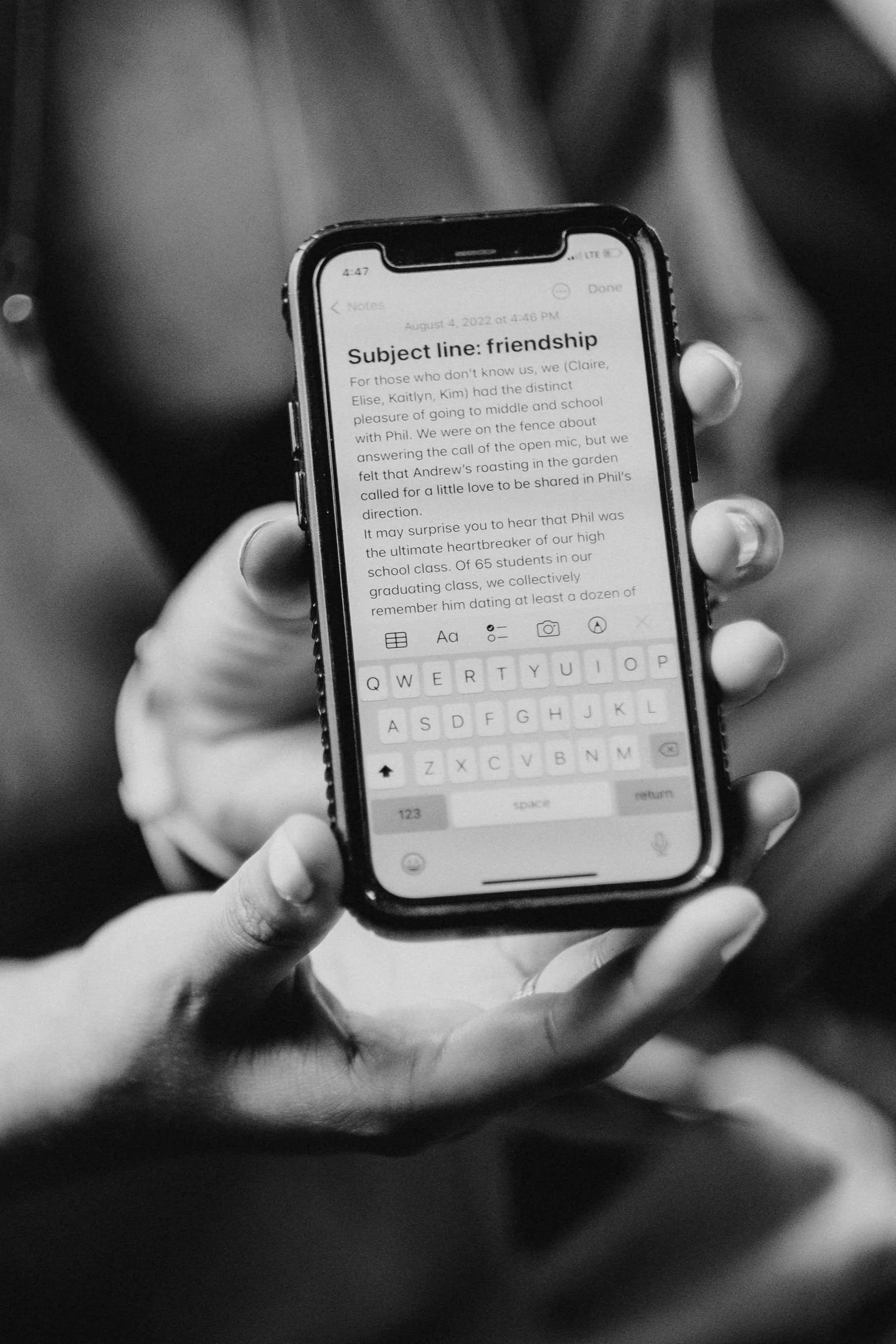 Black and white photo of a hand holding a smartphone displaying a note titled 'Subject line: friendship.'