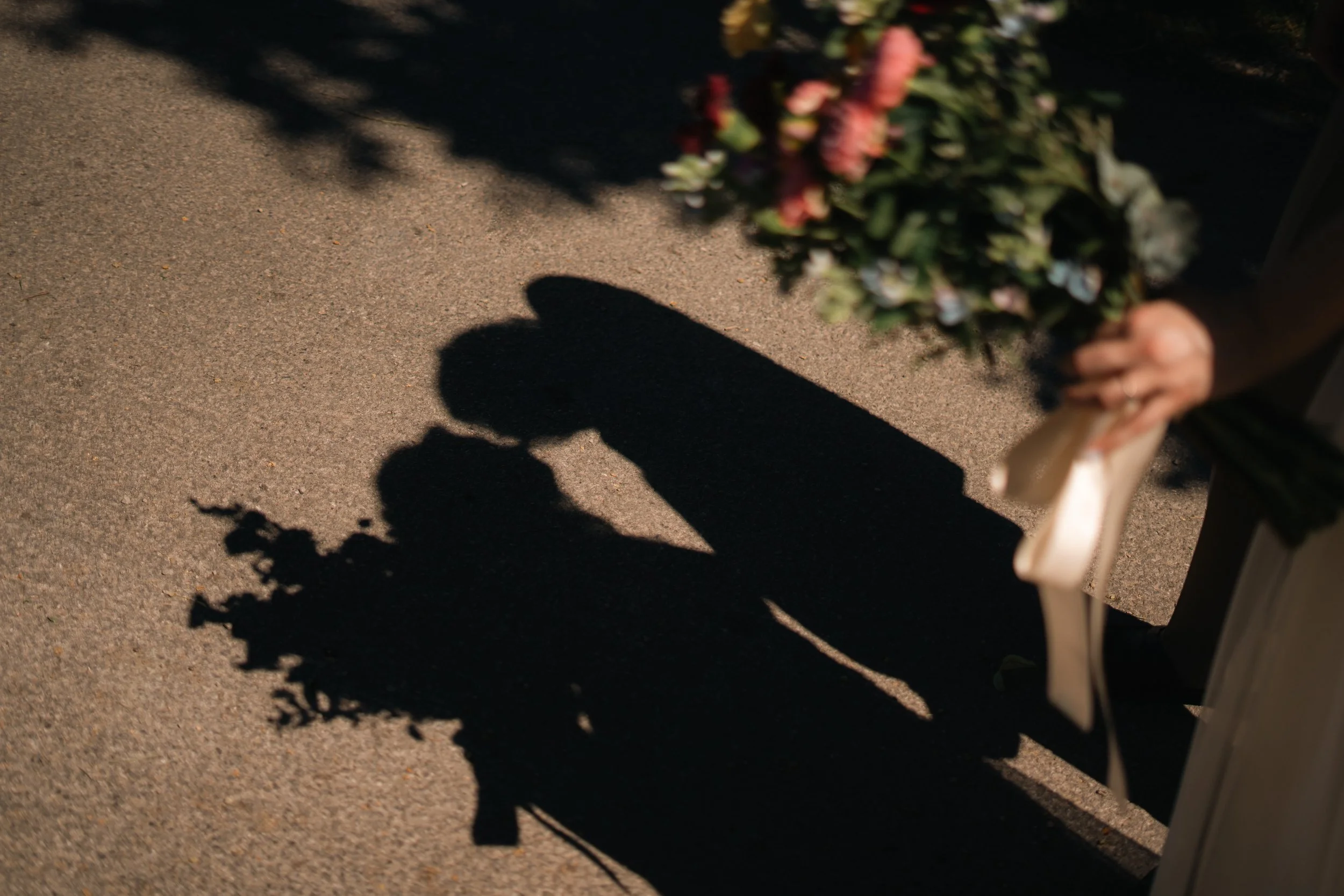 Shadow of a person holding a bouquet of flowers on a sidewalk.