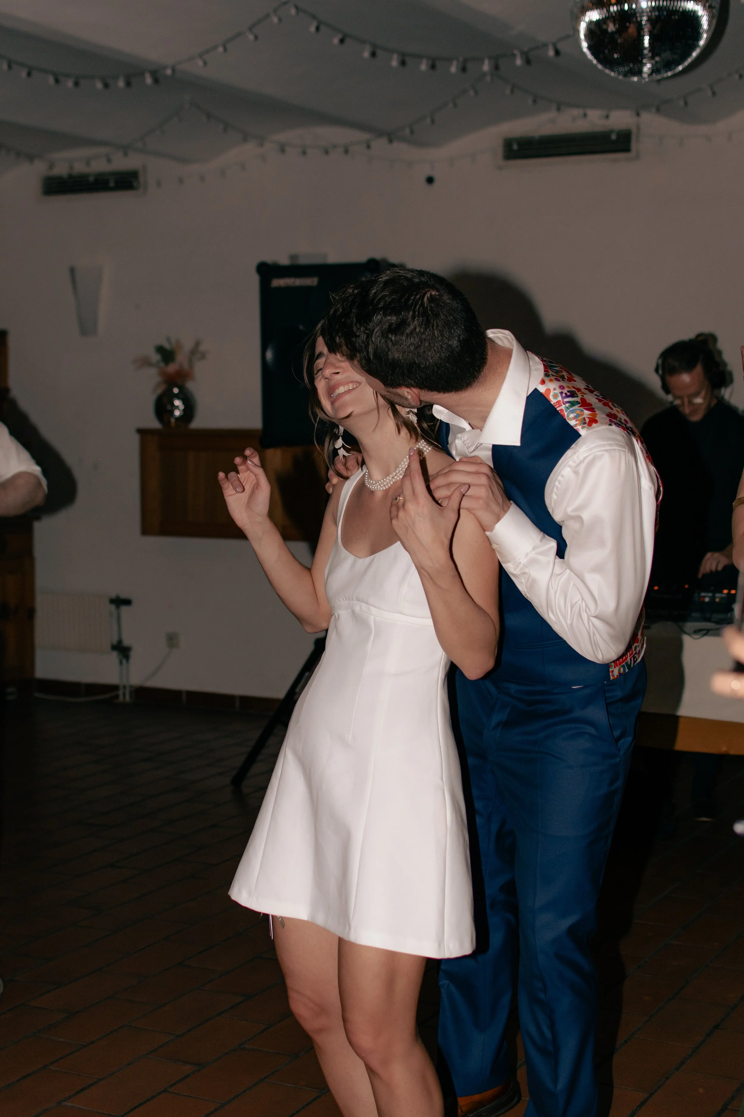 A man and woman dancing happily at a party, with string lights and a disco ball overhead.