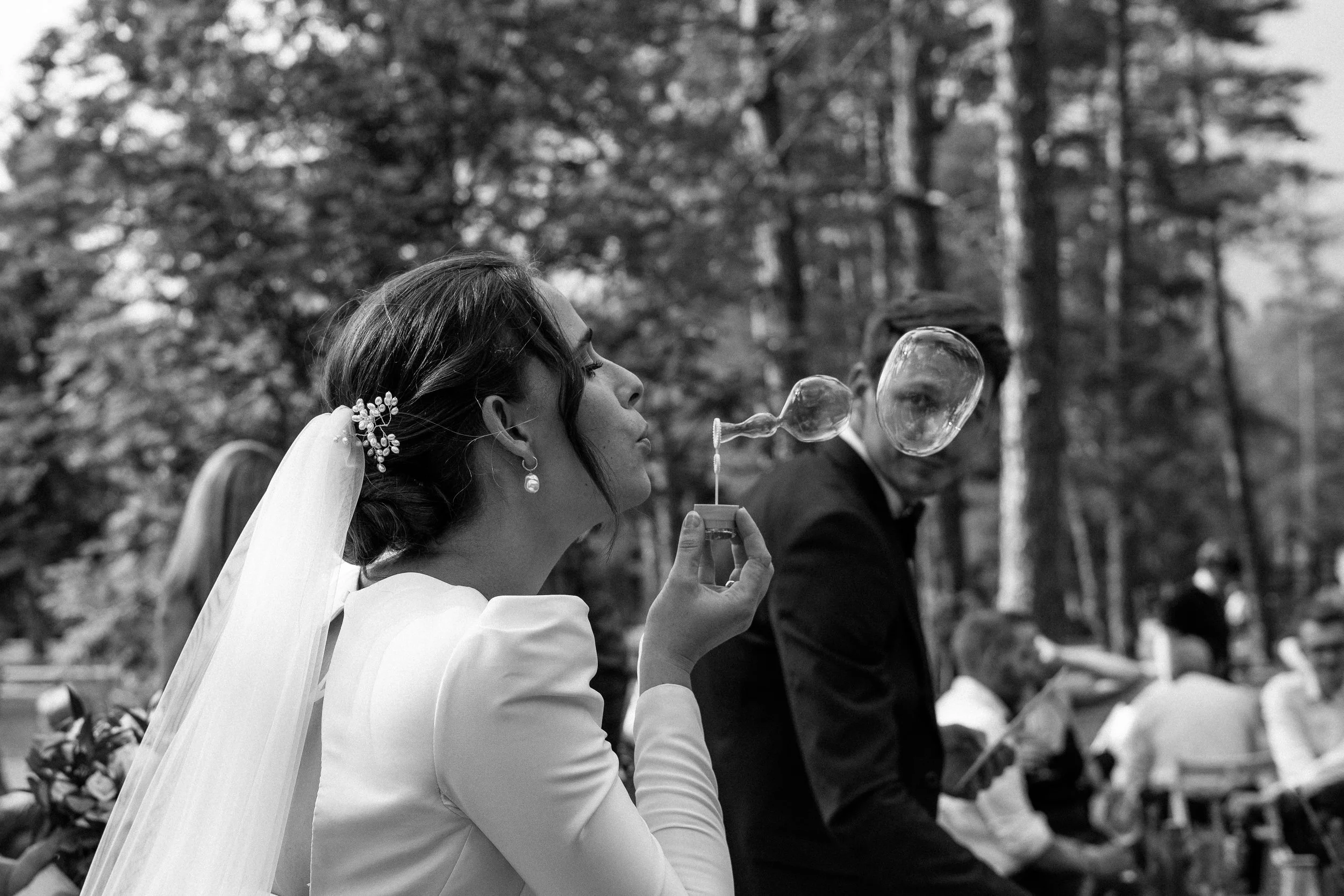 Bride in wedding dress and veil blowing bubbles outdoors during a wedding ceremony.
