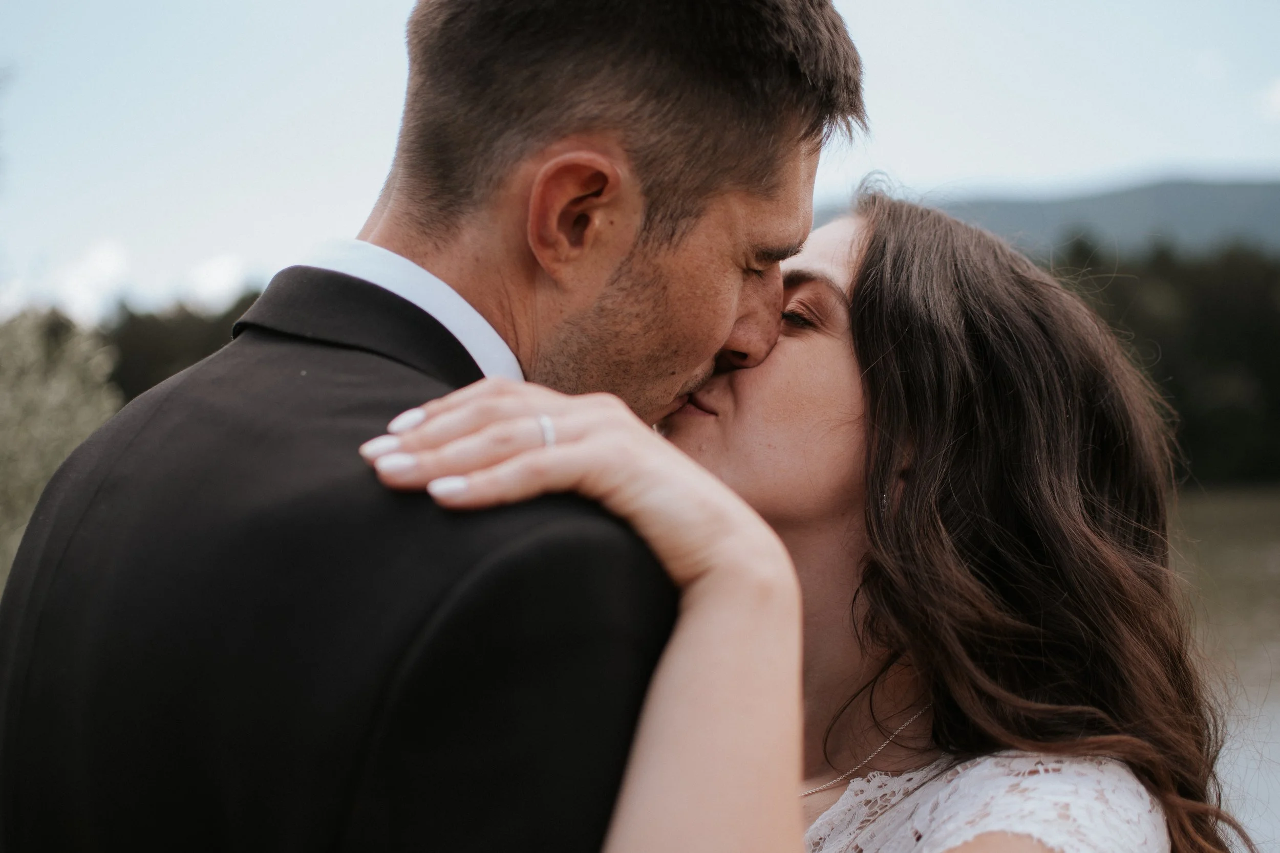 A close-up of a couple kissing outdoors during the daytime, with a blurred natural background.