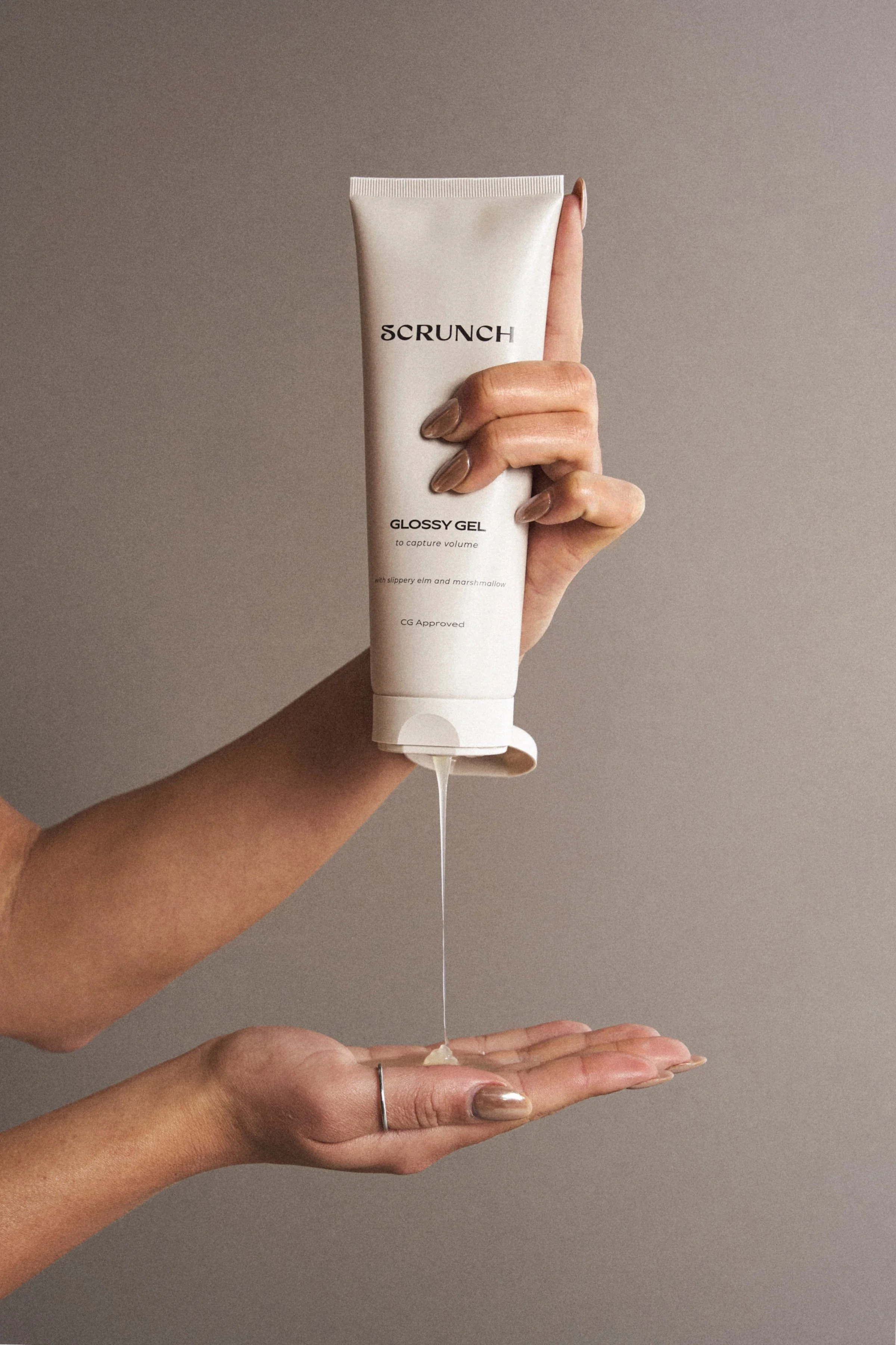 Hand holding a tube of Scrunch Glossy Gel with a gray background