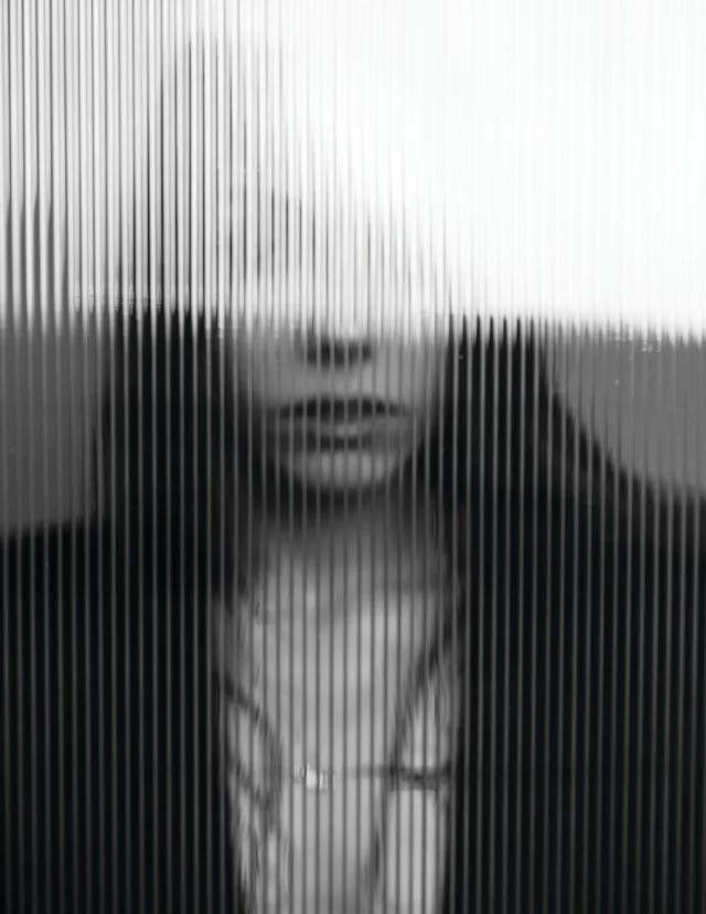 zwart wit foto van jonge vrouw achter geribbeld glas