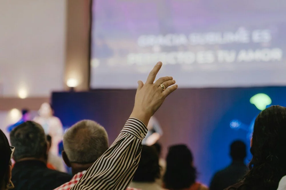 Congregation member raising a hand during a church worship service with song lyrics projected on a screen.