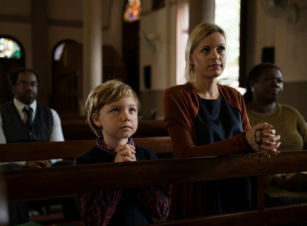 Young boy and woman praying together in church pews during a worship service.