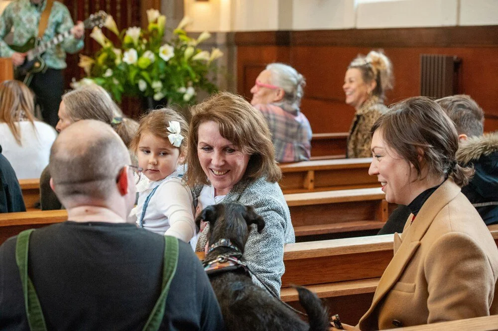 Families and children sitting together in church pews during a service, smiling and interacting in a warm community setting.