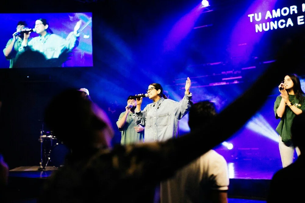 Worship team leading a live church service on stage with congregation members raising hands in praise.