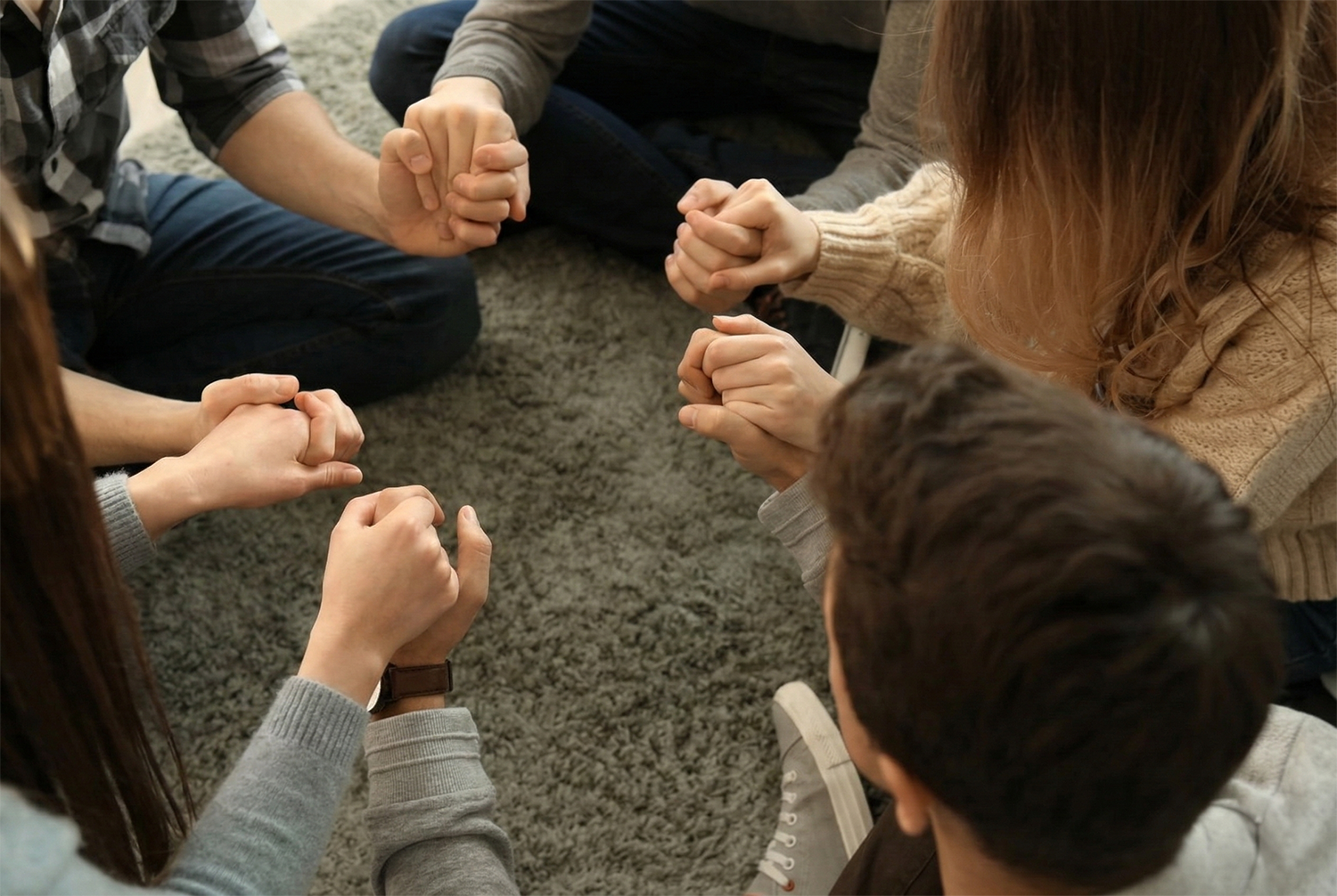 Parents and teens holding hands in prayer during a family faith moment at home