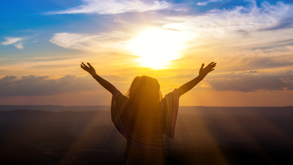 Person worshiping at sunrise symbolizing faith, hope, and connection with God through Christ.