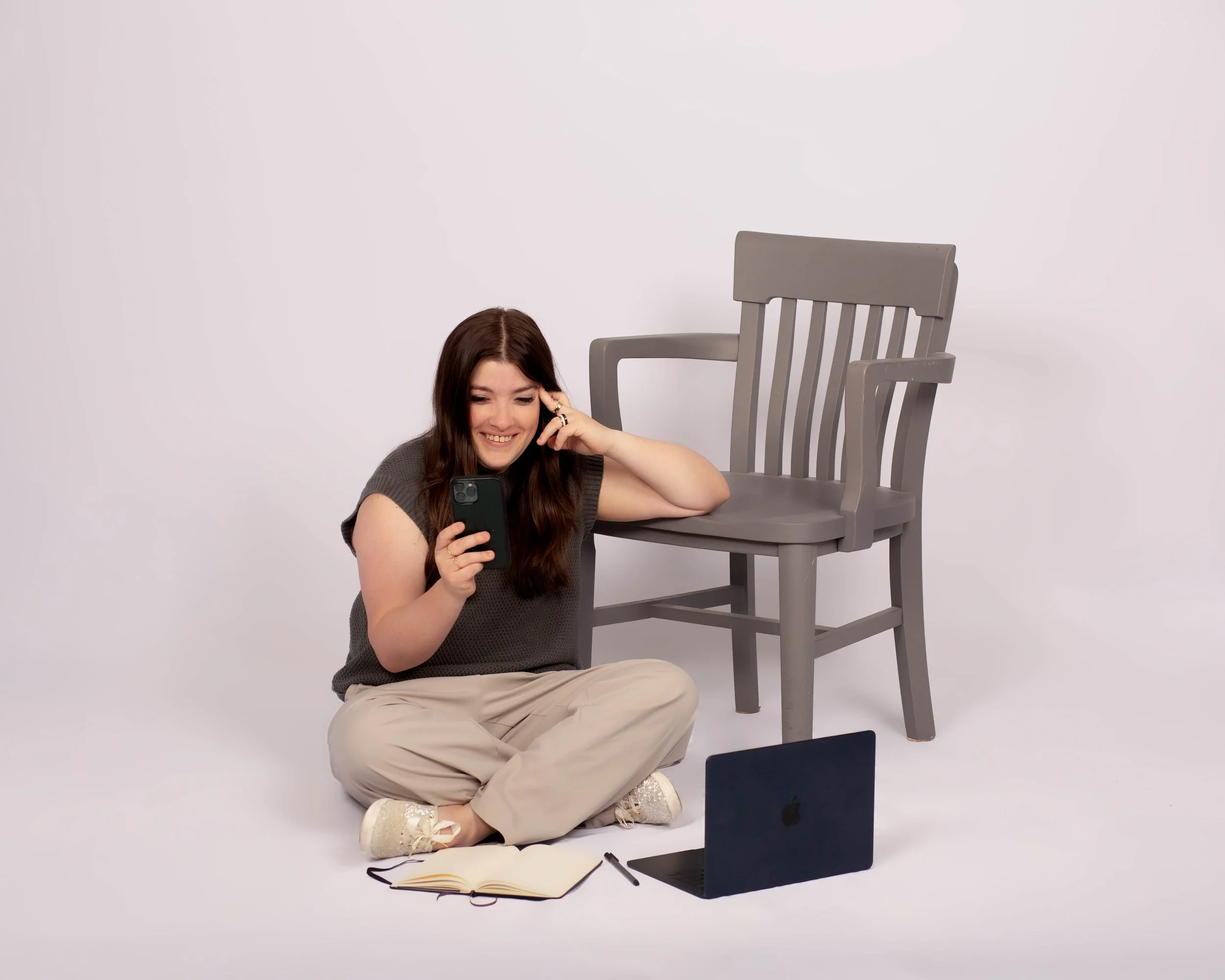 woman sits on floor looking at phone with laptop and notebook open