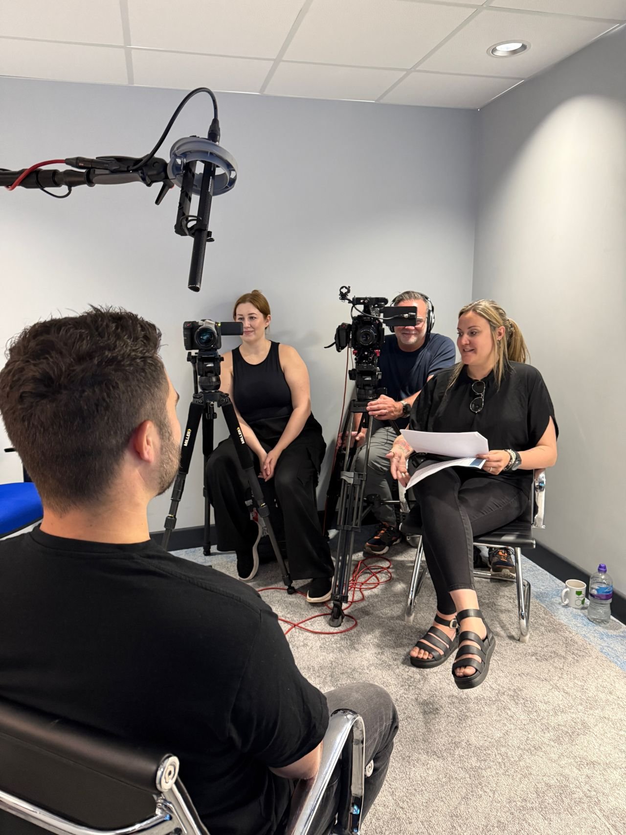 The ID2 crew participating in a video interview or recording session in a small room, with one person being filmed and others sitting nearby with recording equipment.
