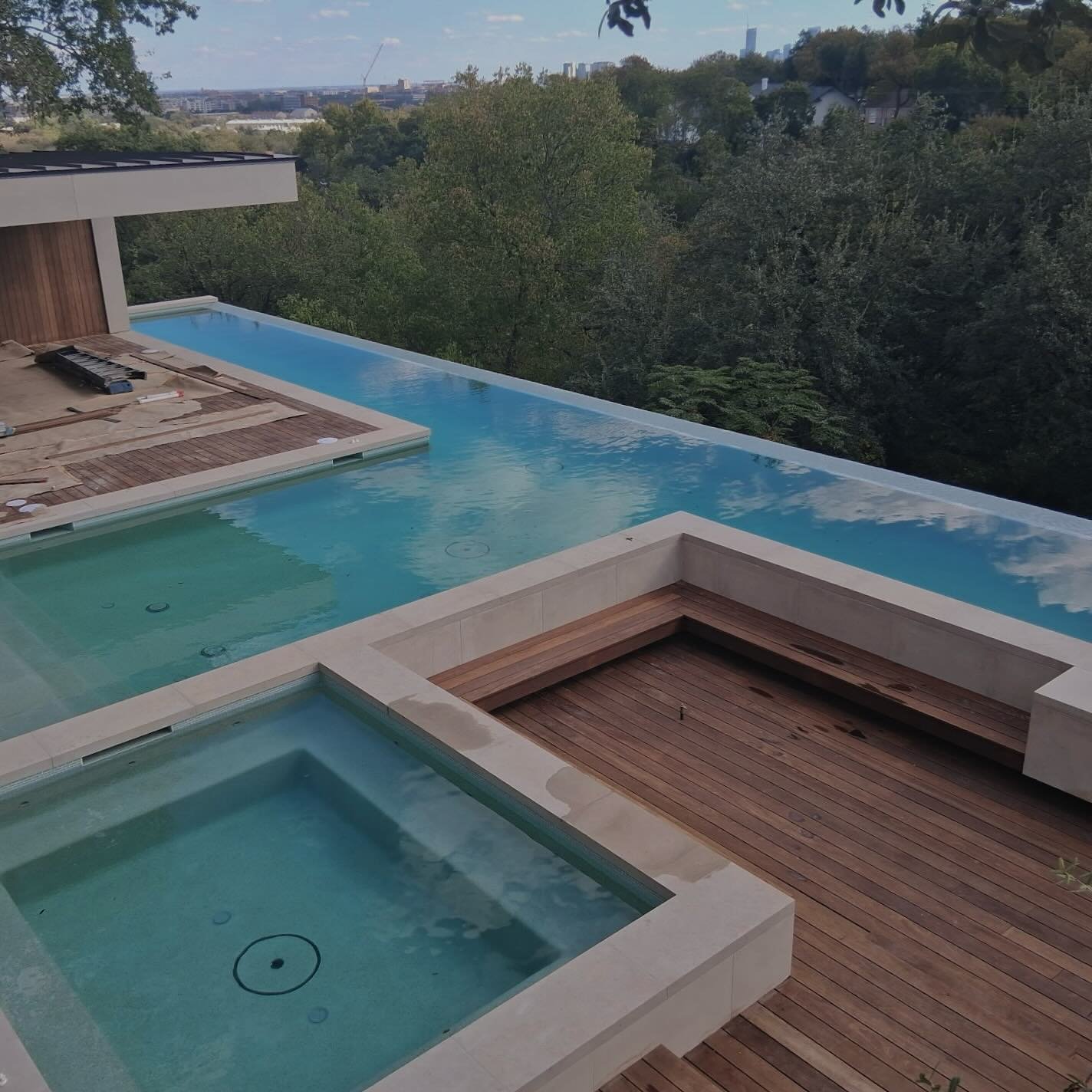 The calm before the first swim. 
Freshly plastered and filled &mdash; this hillside infinity pool now reflects the skyline and treetops beyond. The soft, glassy hue comes from NPT Mini Pebble Jade, a perfect complement to the limestone coping, glass 