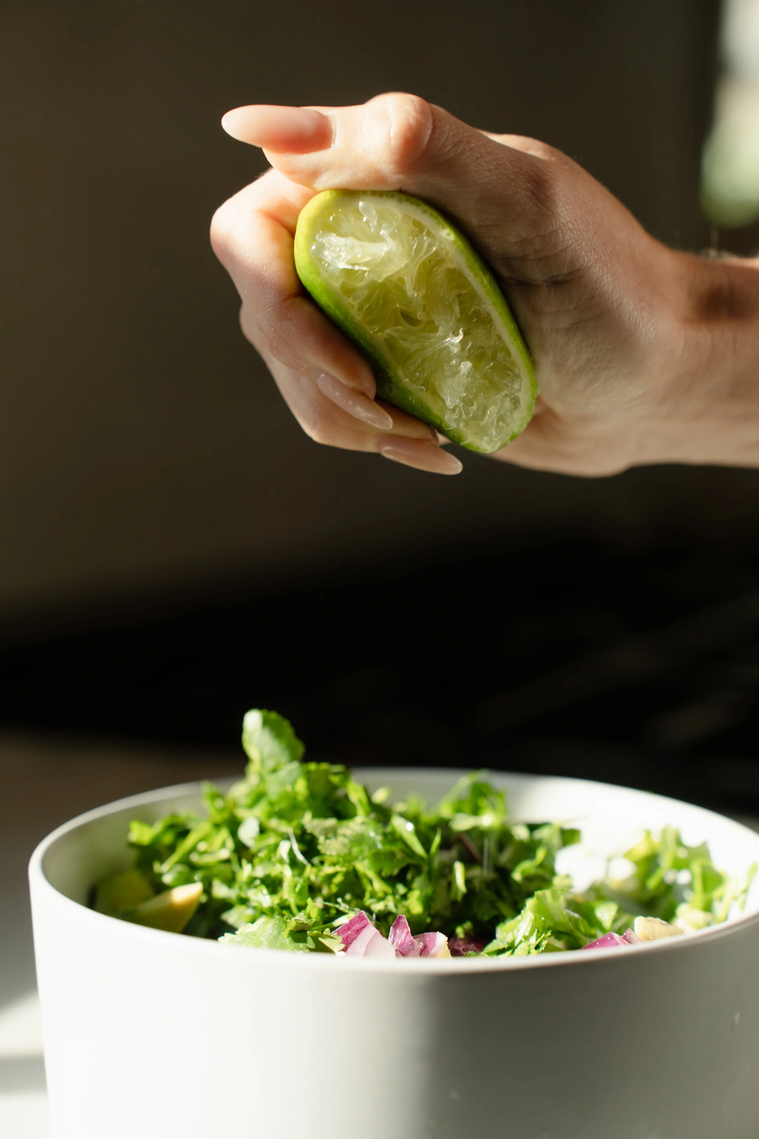 A person squeezing lime juice over a bowl of salad containing chopped greens and vegetables.