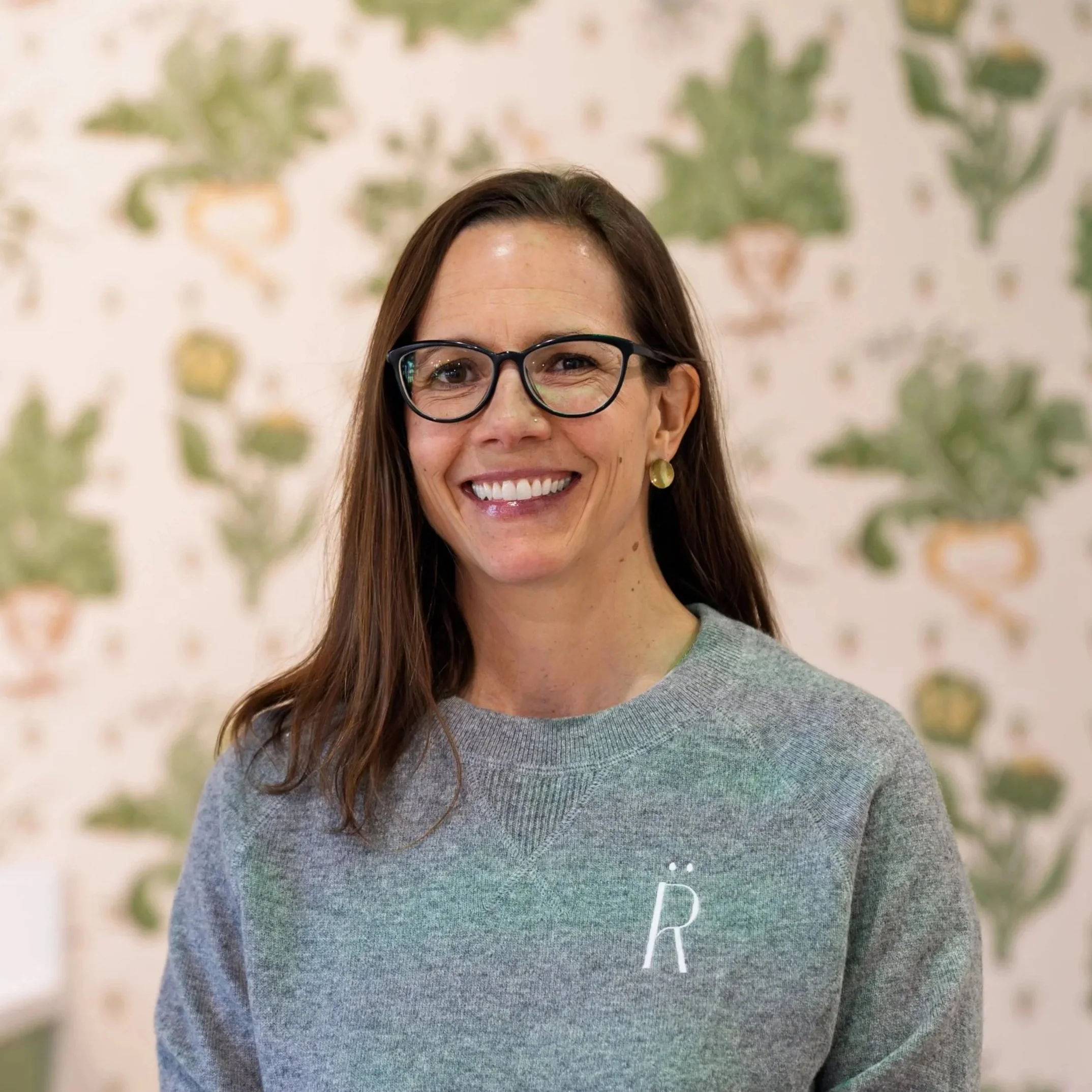 A woman with long brown hair wearing an orange polo shirt with Virginia embroidered on it, smiling against a gray background.
