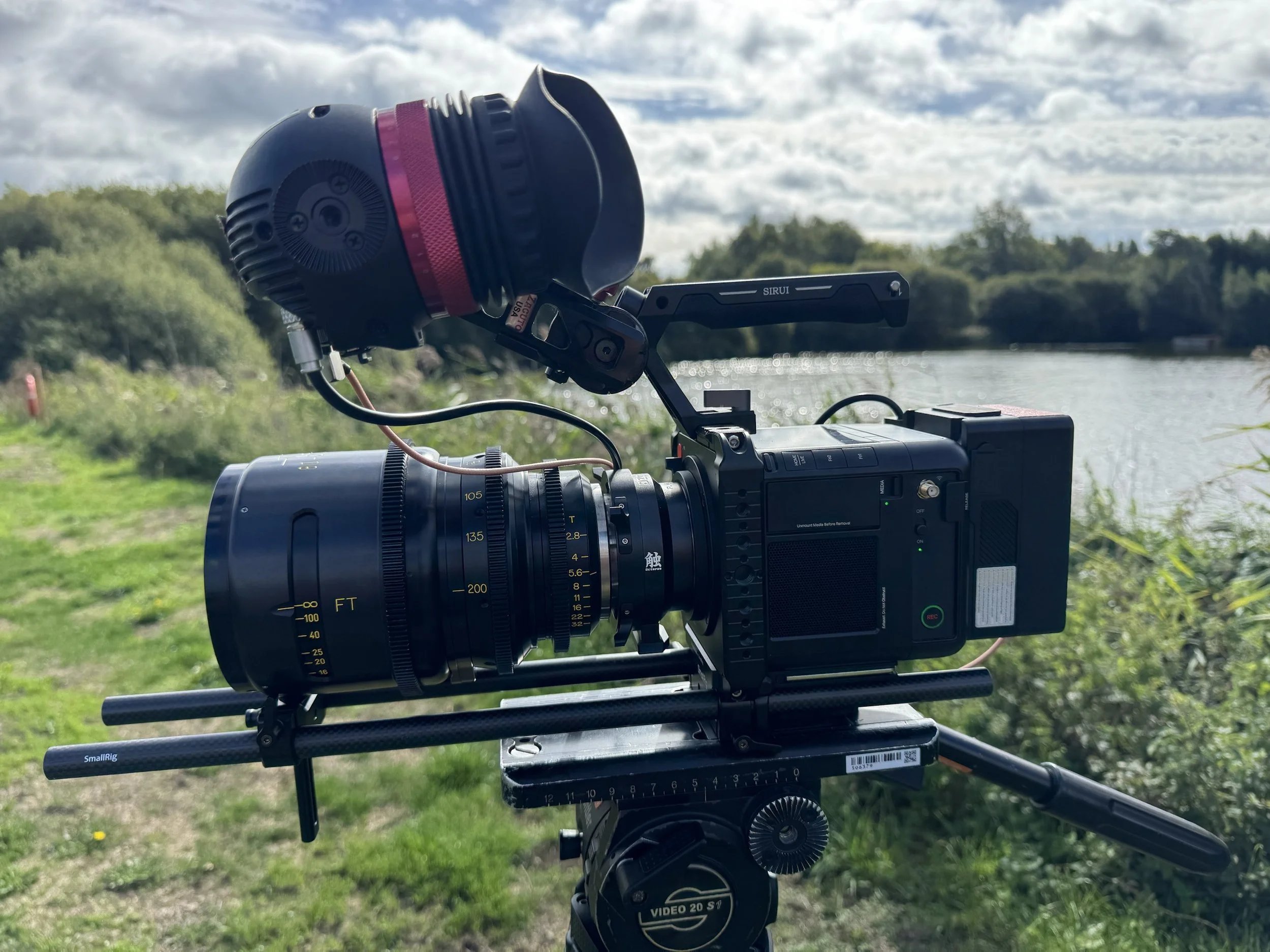 Pixboom Spark high-speed slow-motion camera with cine zoom lens, on a tripod beside a lake