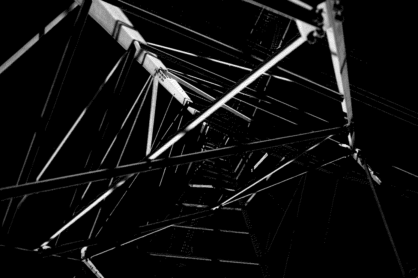 Black and white photo of a metal scaffolding structure, viewed from below, extending upward into darkness.