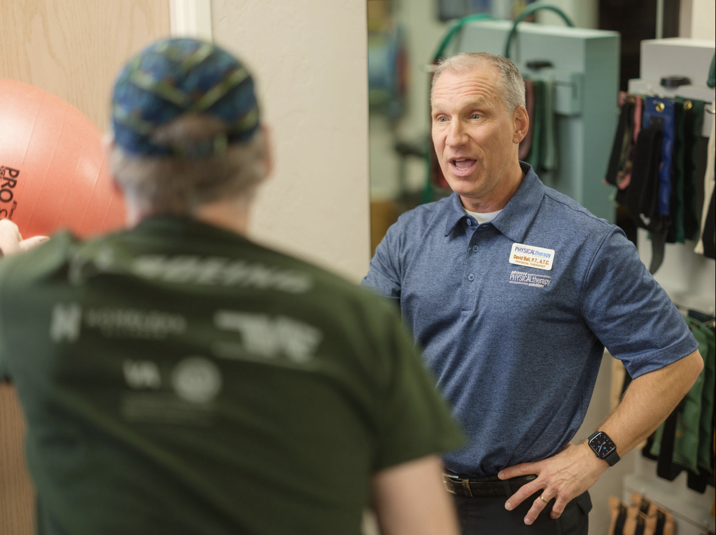 A physical therapist guides a patient through an exercise using a stability ball during a rehabilitation session.