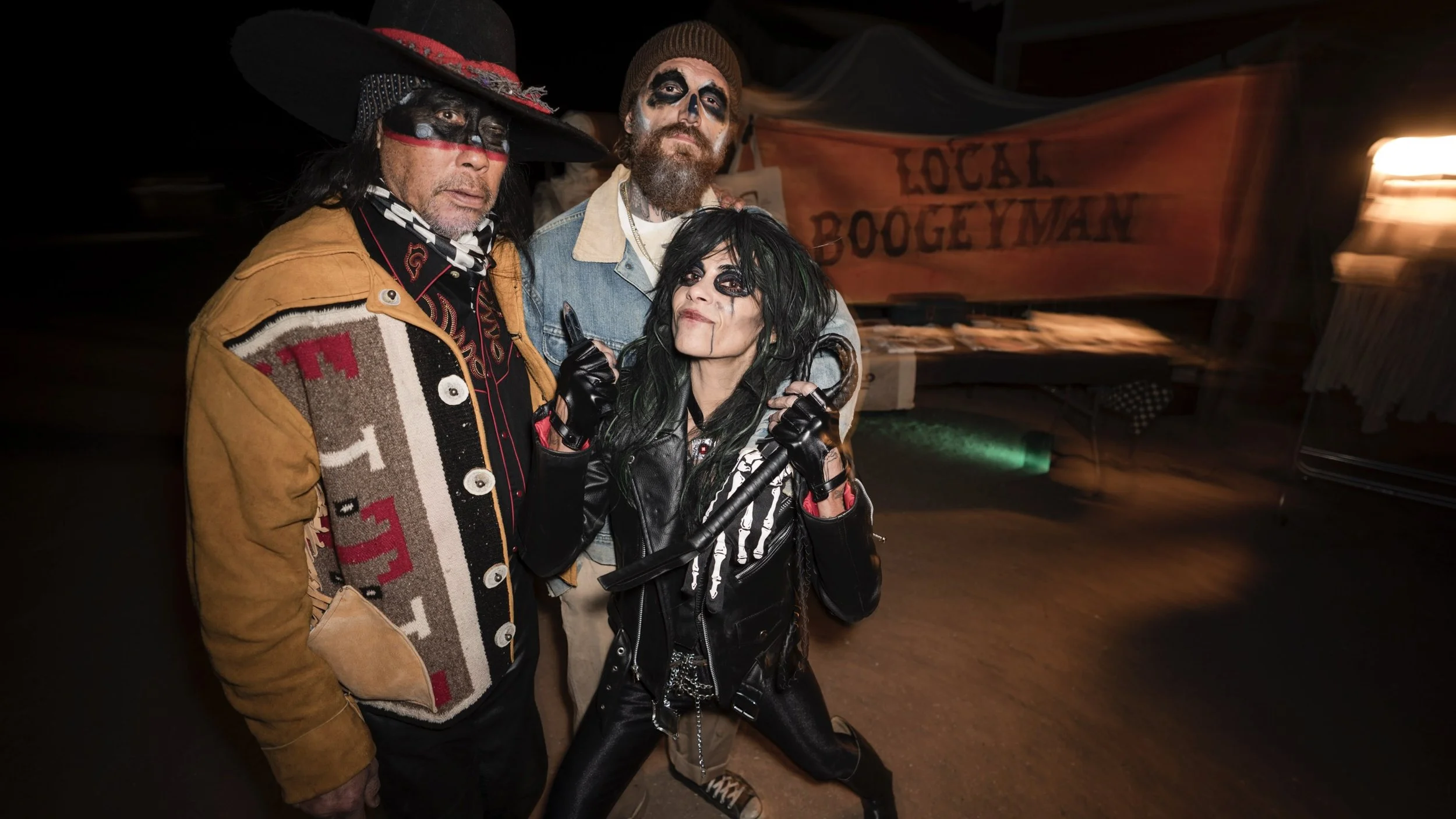 Three people dressed in punk and rock costumes, standing together outdoors at night, with a banner reading 'Local Boogeyman' in the background.