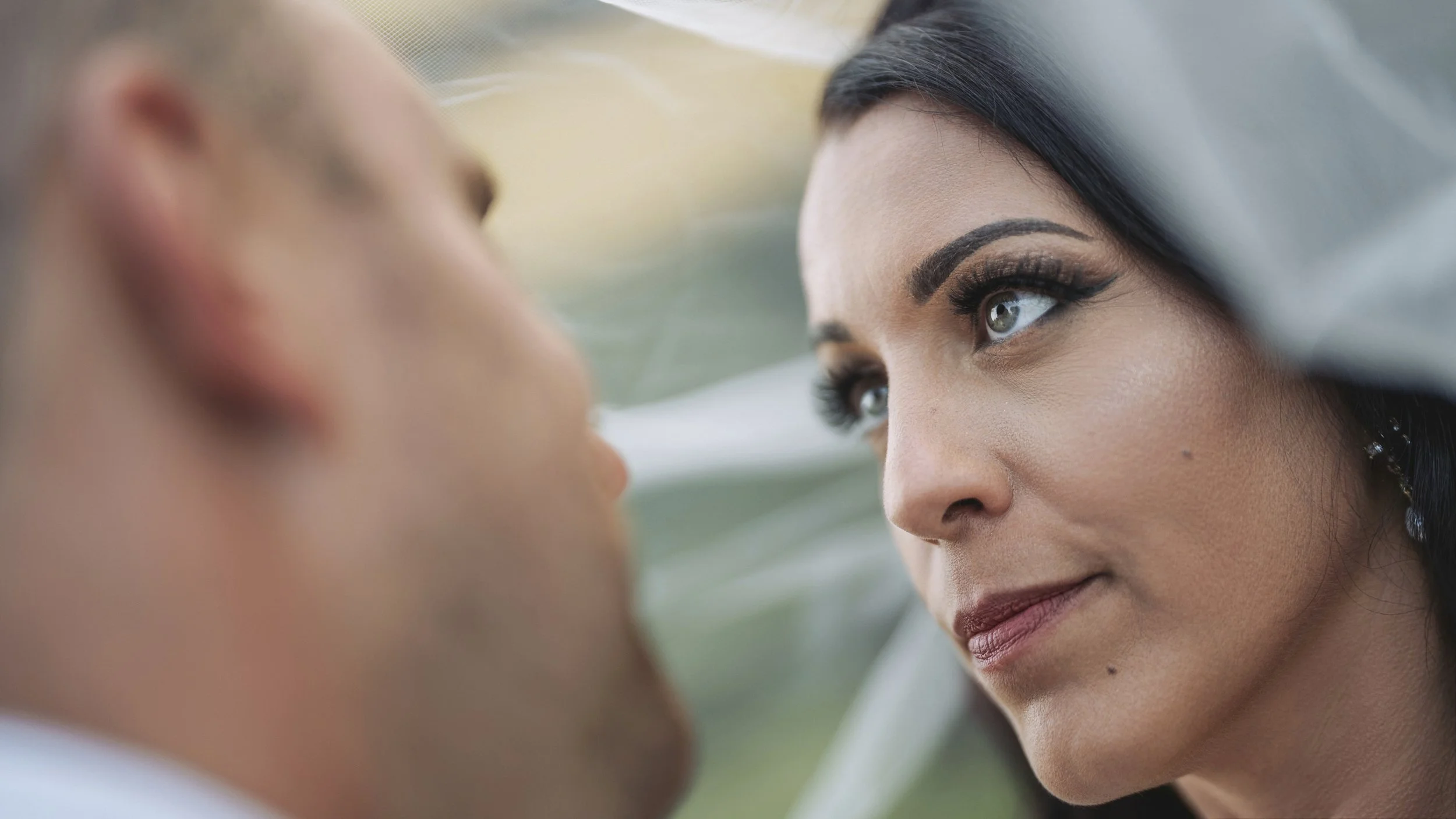 Close-up of a woman looking intensely at a man, both with blurred background and soft lighting.