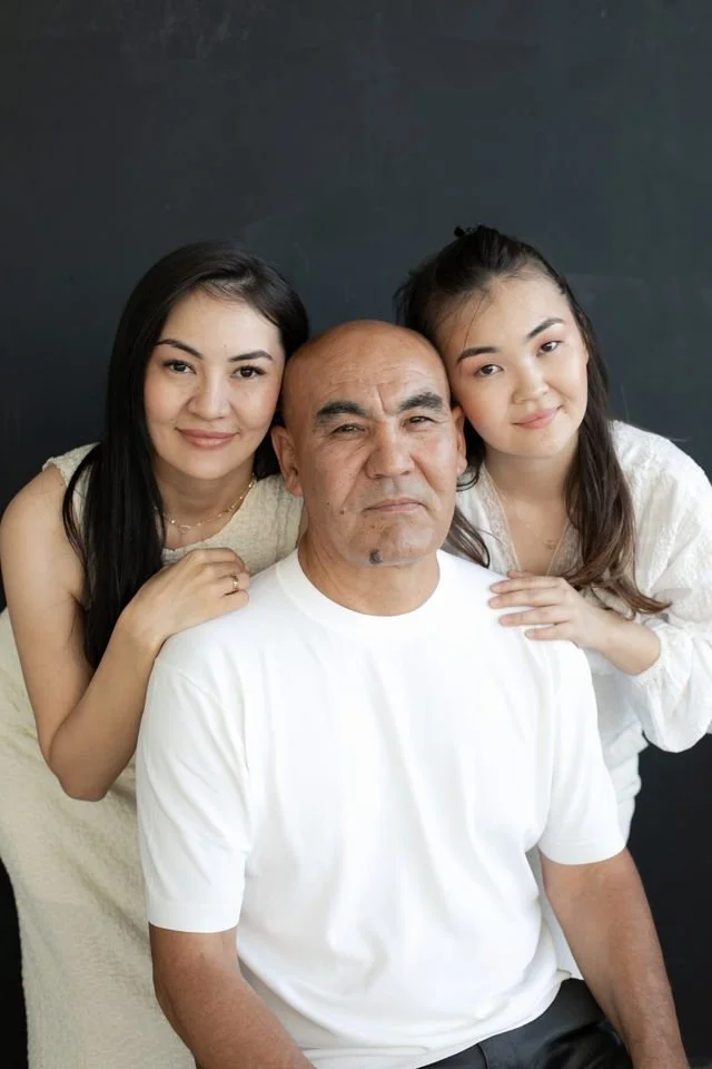 A man sitting in front with two women standing behind him, all smiling and close together against a dark background representing counseling for depression, anxiety, stress, and relationship challenges for asian americans.