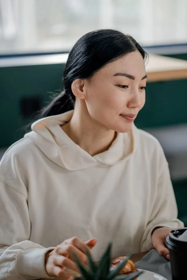 An Asian American female adult smiling into the distant in a room representing counseling services for depression for Asian Americans in Oregon and California.