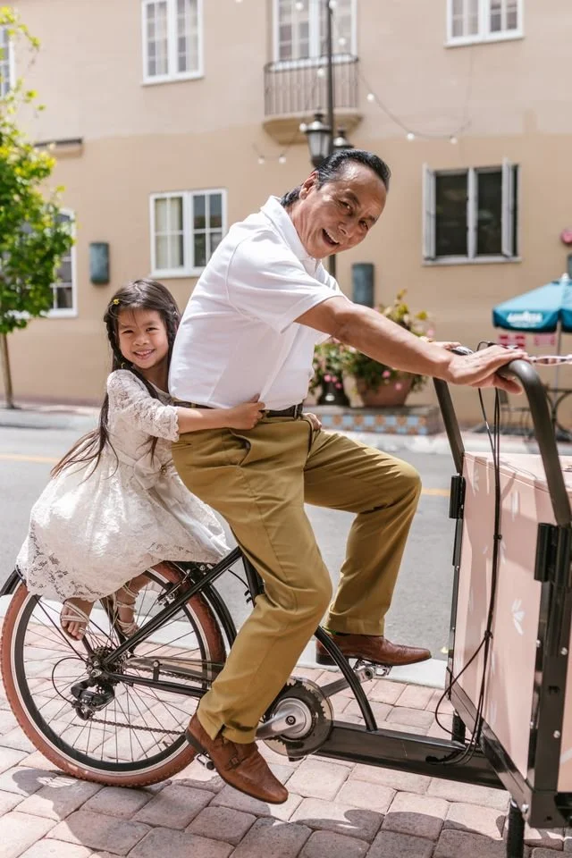 A man and a young girl riding a tandem bike together on a street, smiling and enjoying the sunny day representing a Korean therapist in Portland providing counseling for depression, anxiety, stress, and relationship challenges for Asian Americans.