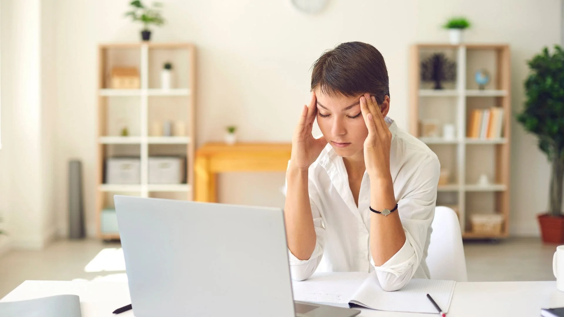 A woman sitting at her desk with her fingers on her temples.