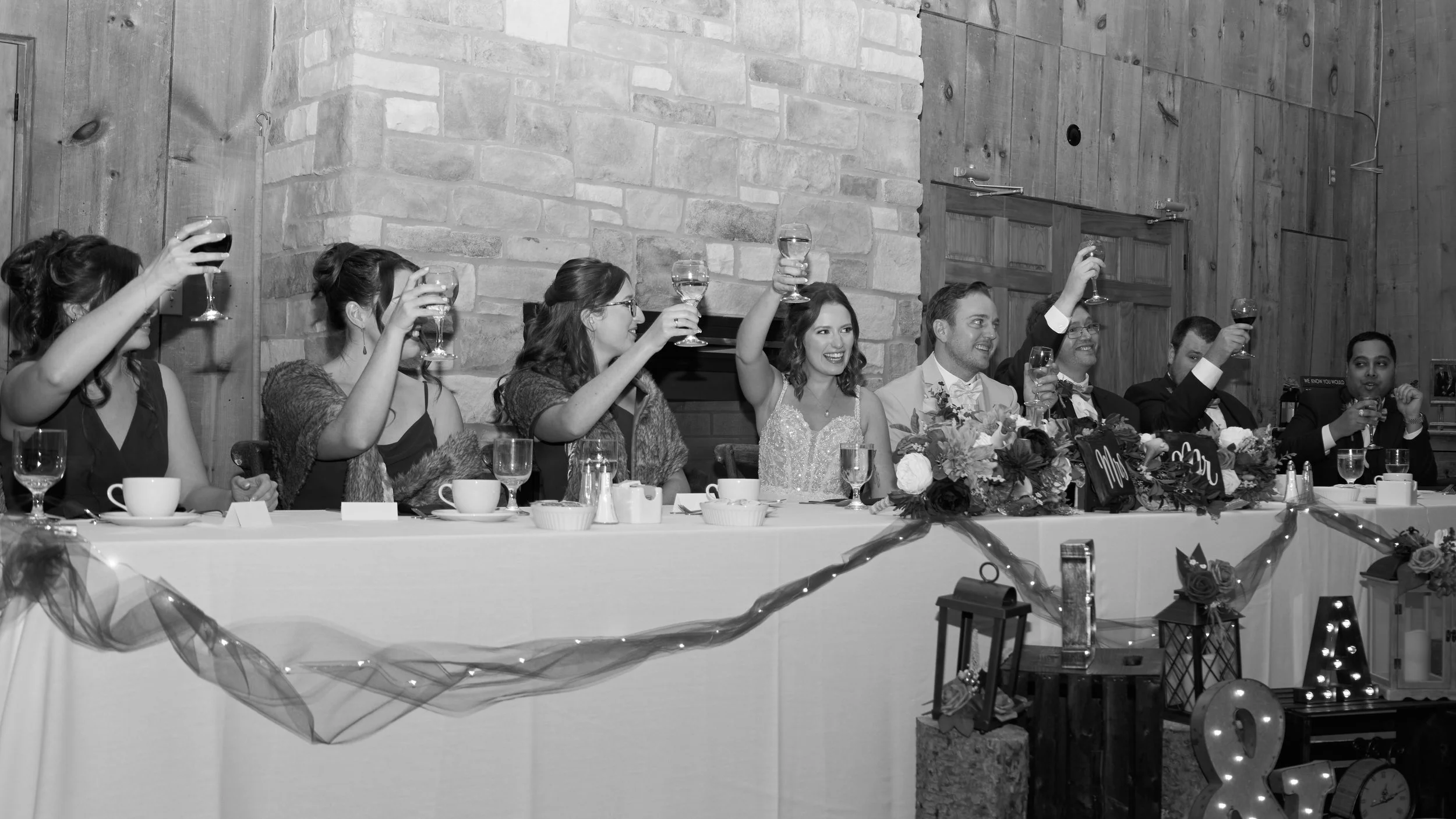Group of people sitting at a table, raising glasses for a toast at a wedding reception.