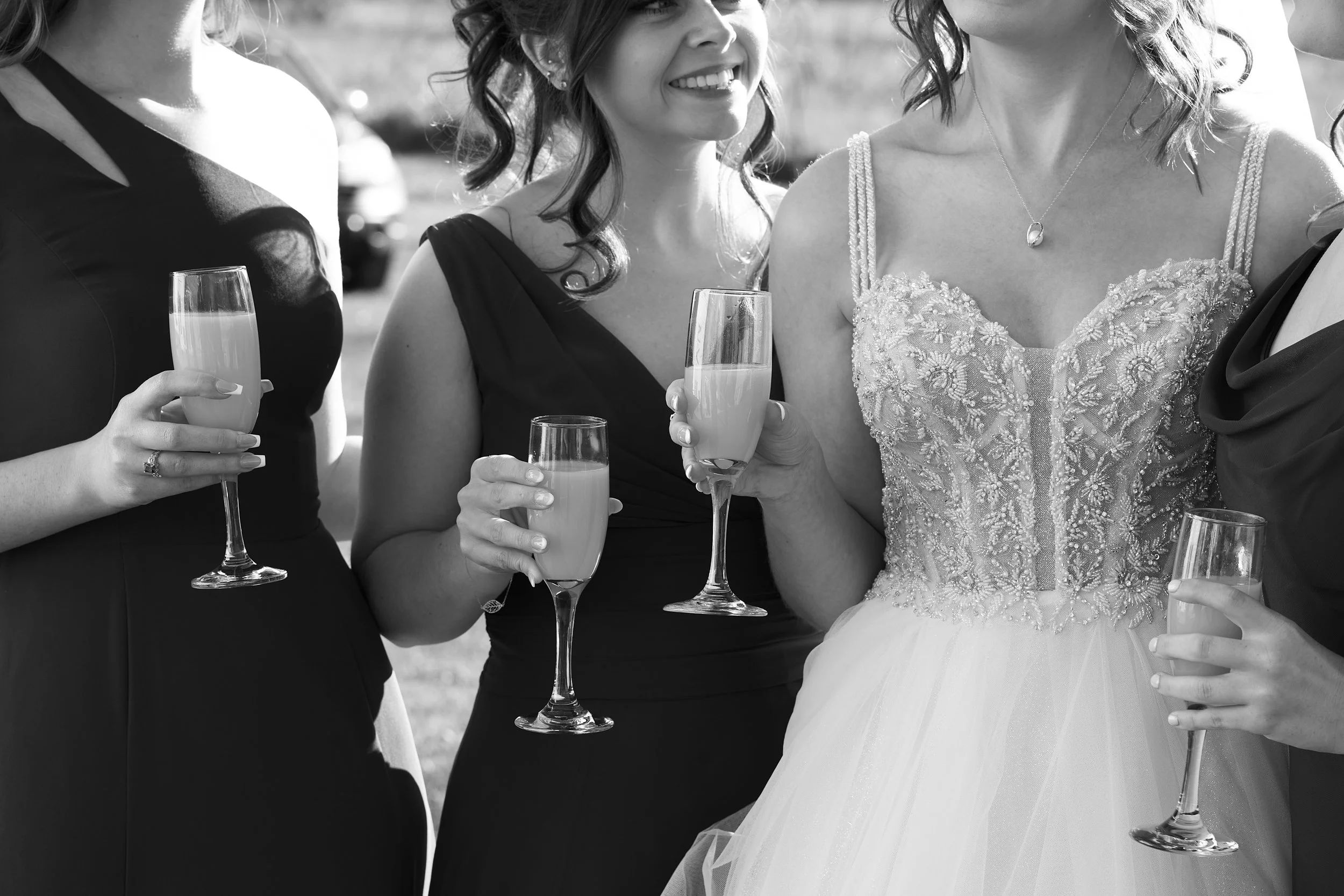 A group of women at a wedding celebration holding glasses of champagne, with the bride in a detailed lace wedding gown and the women in evening dresses.