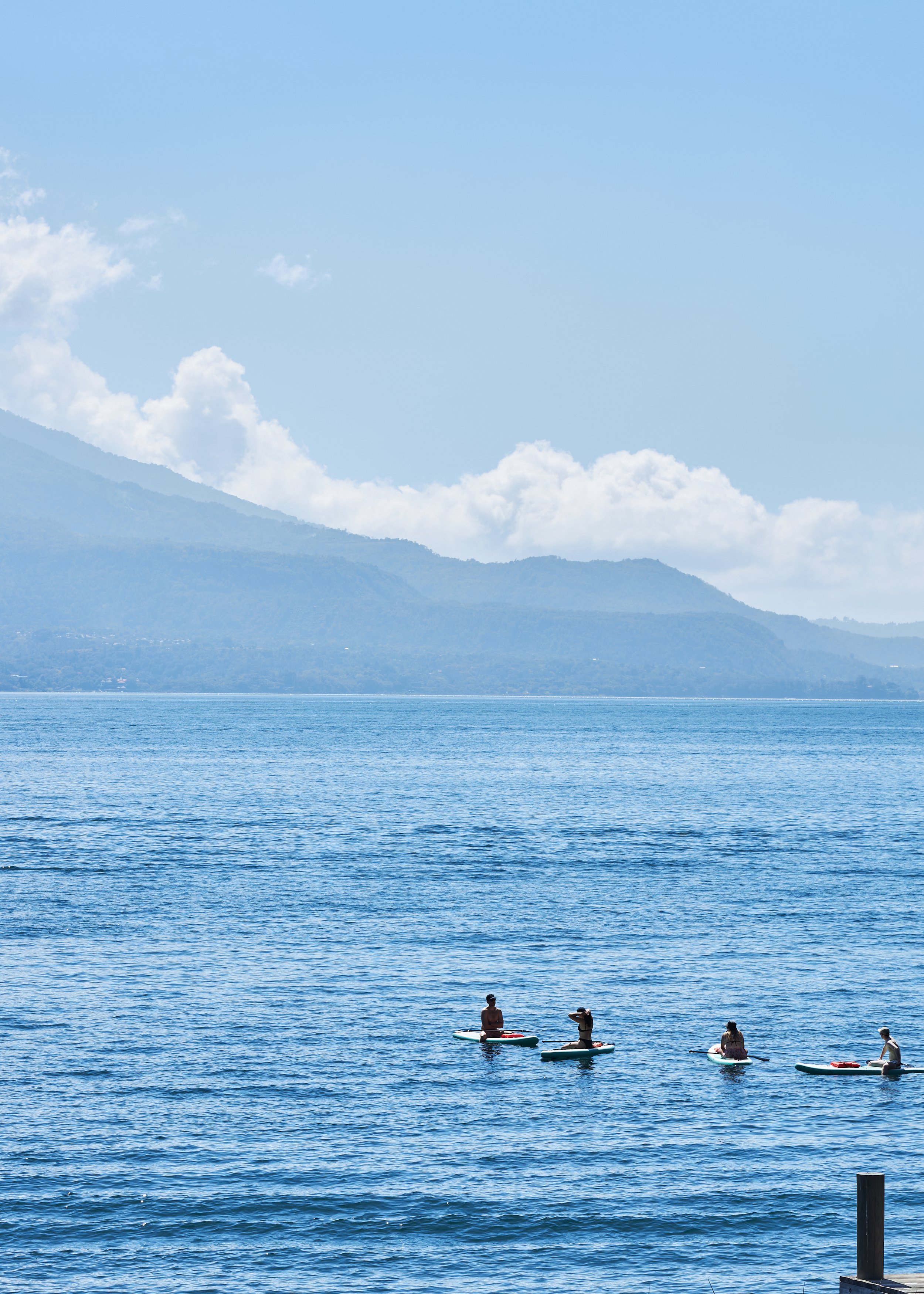 Four people on paddleboards on a calm lake with mountains and clouds in the background.
