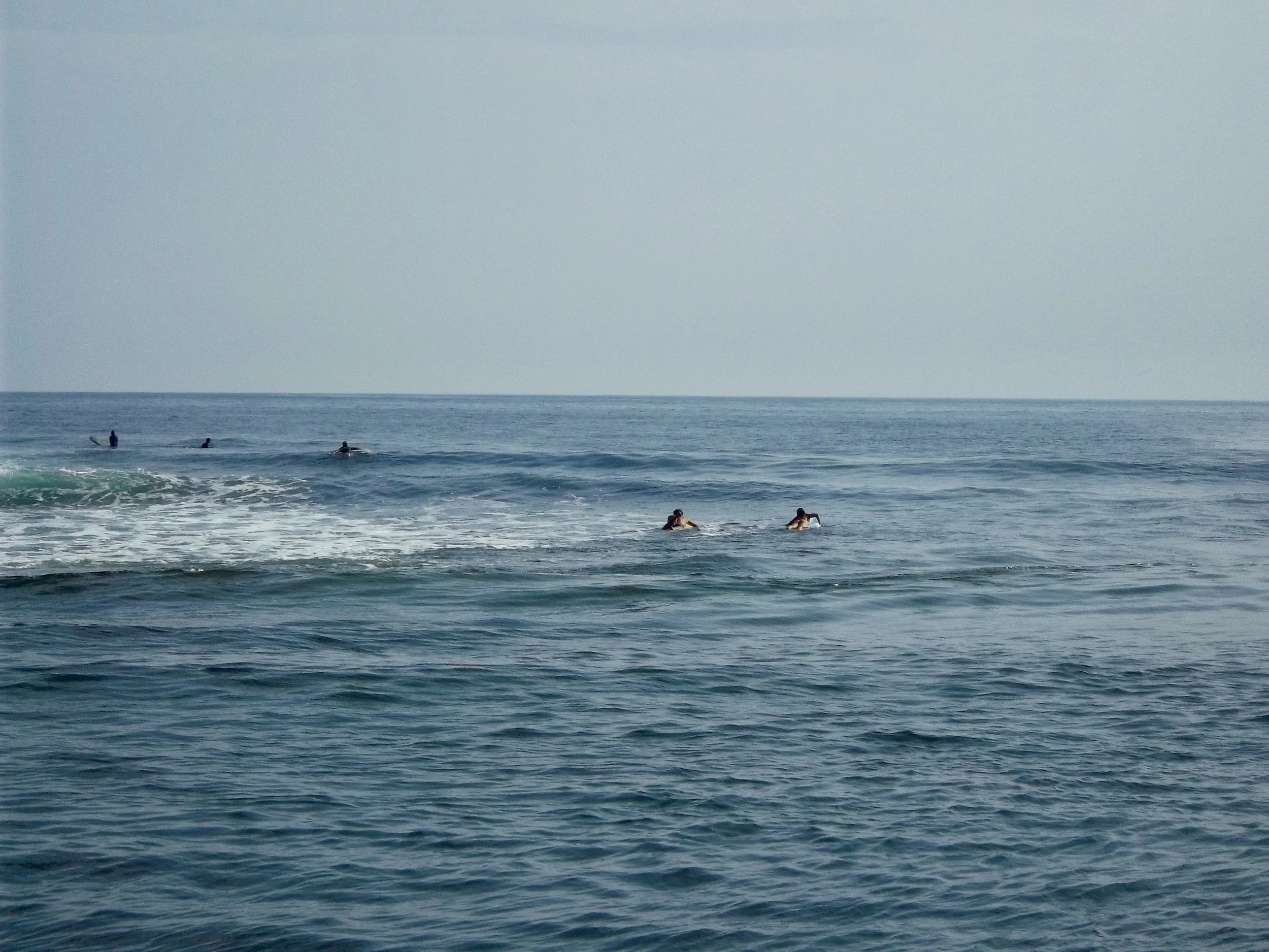 People surfing and swimming in the ocean on a clear day with calm waves.