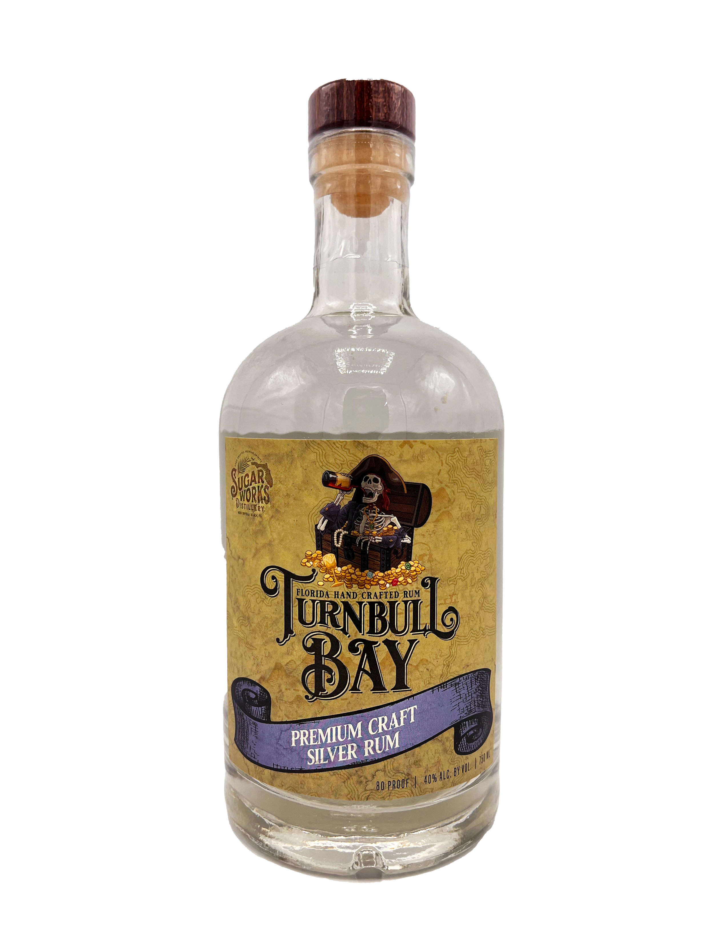 A clear glass bottle of Turnbull Bay Premium Craft Silver Rum produced by Sugar Works Distillery, with a wooden cap and a colorful label featuring a skeleton pirate with a telescope, treasure, and gold coins.