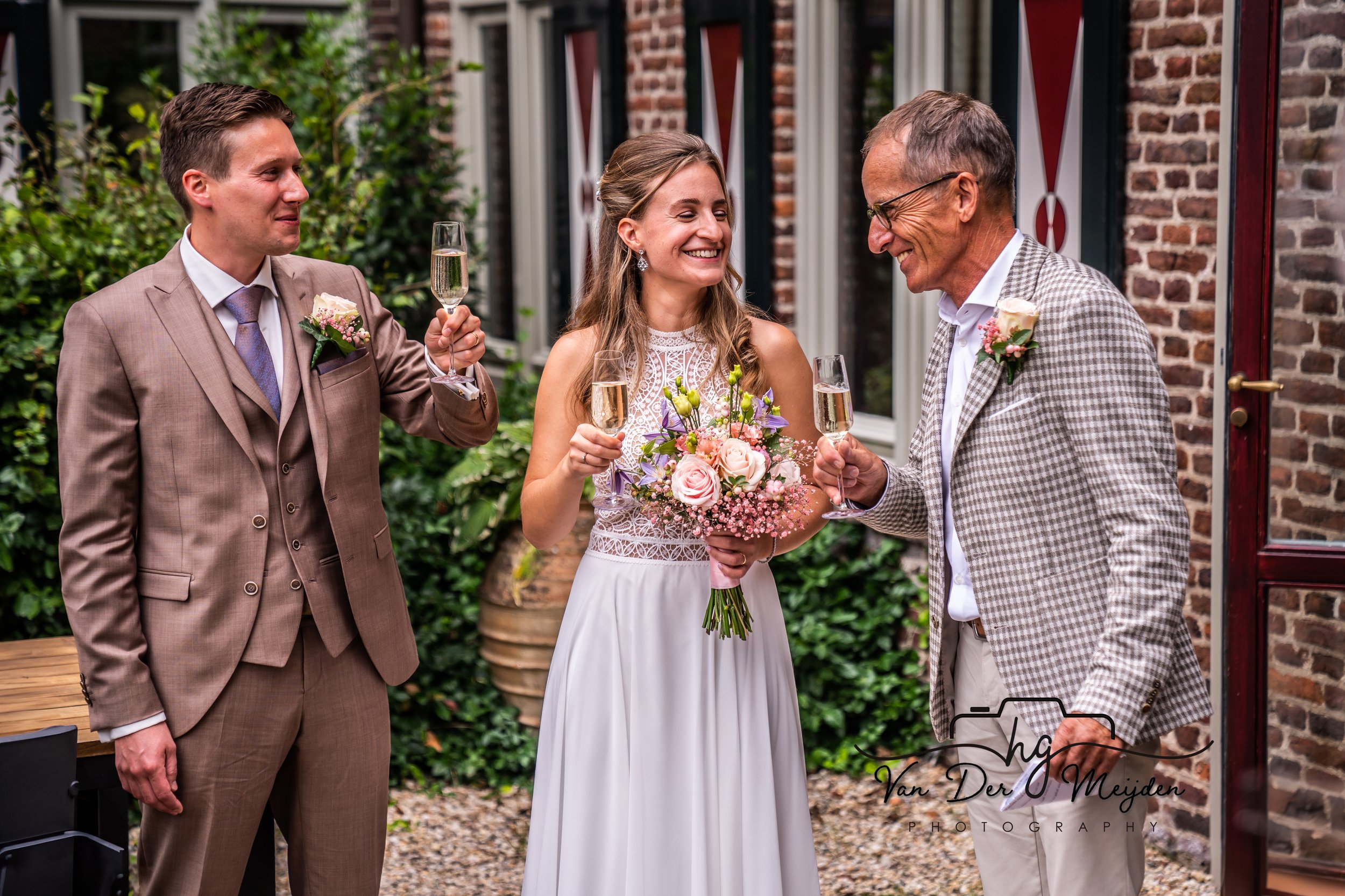 Drie mensen lachen en proosten met champagne; een bruid in een witte jurk met een bruidsboeket, en twee mannen, een in een pak en een in een geruite blazer.