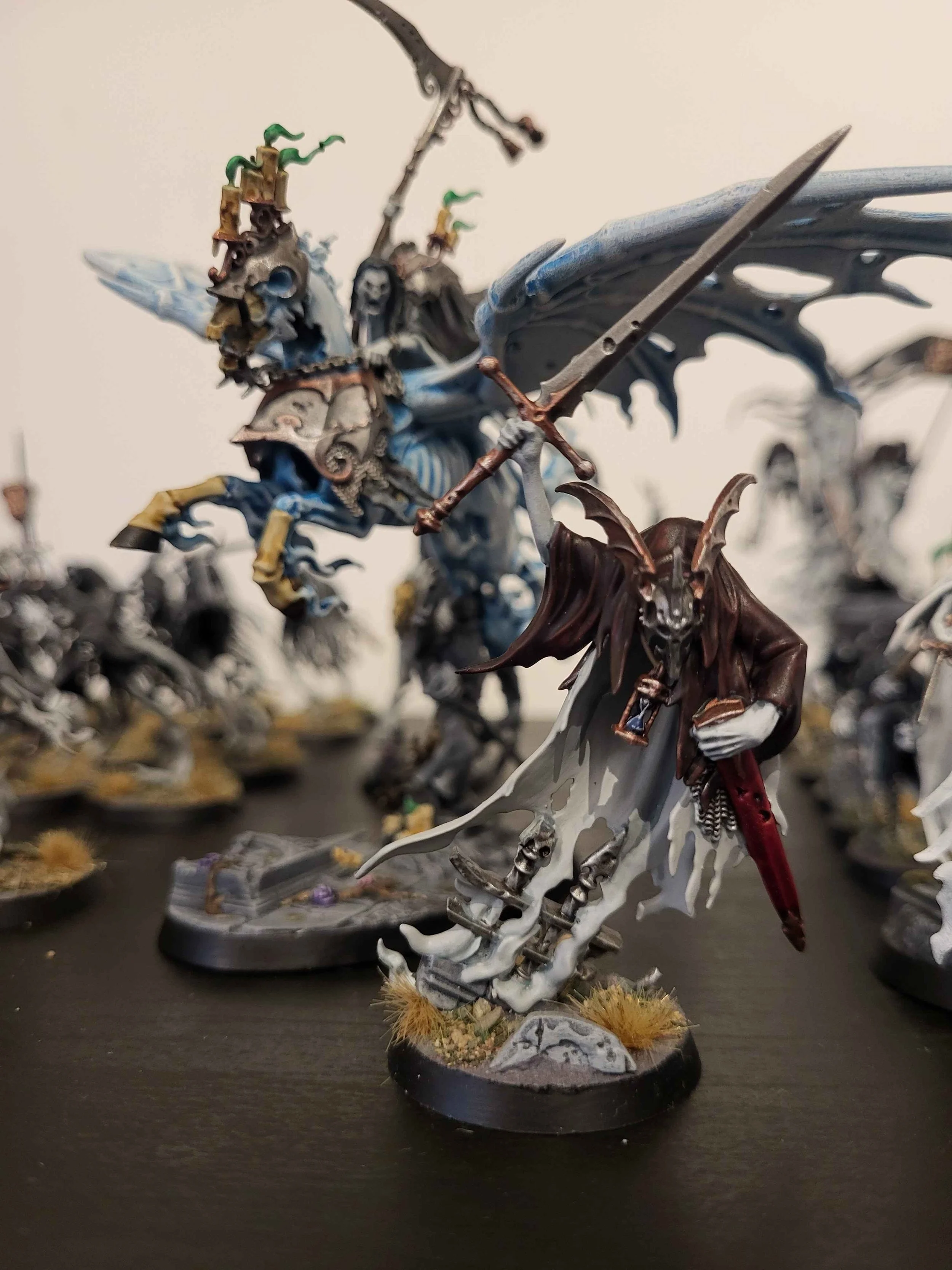 Fantasy tabletop miniature figures depicting winged demons or monsters with detailed armor and weapons, painted in dark and muted colors, arranged on a flat surface.