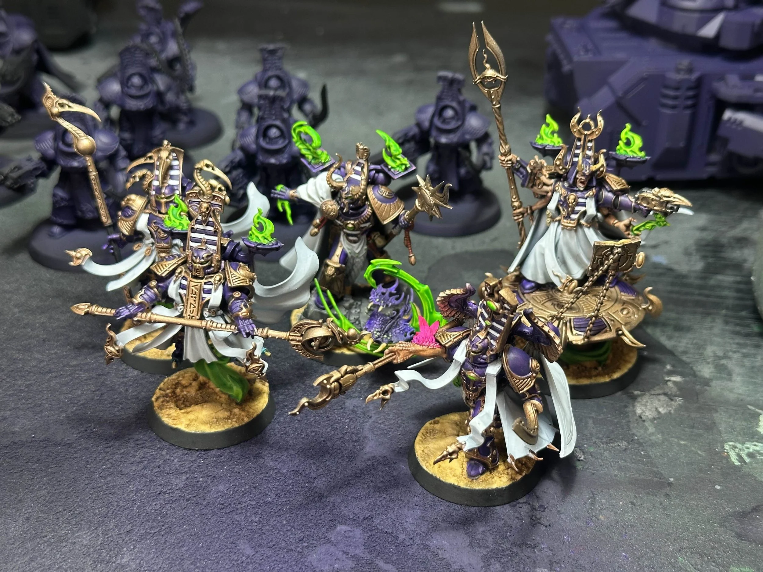 Collection of painted miniature figurines from a tabletop game, depicting armored, fantasy-style characters with glowing green accents and ornate weapons, on a textured gaming surface.