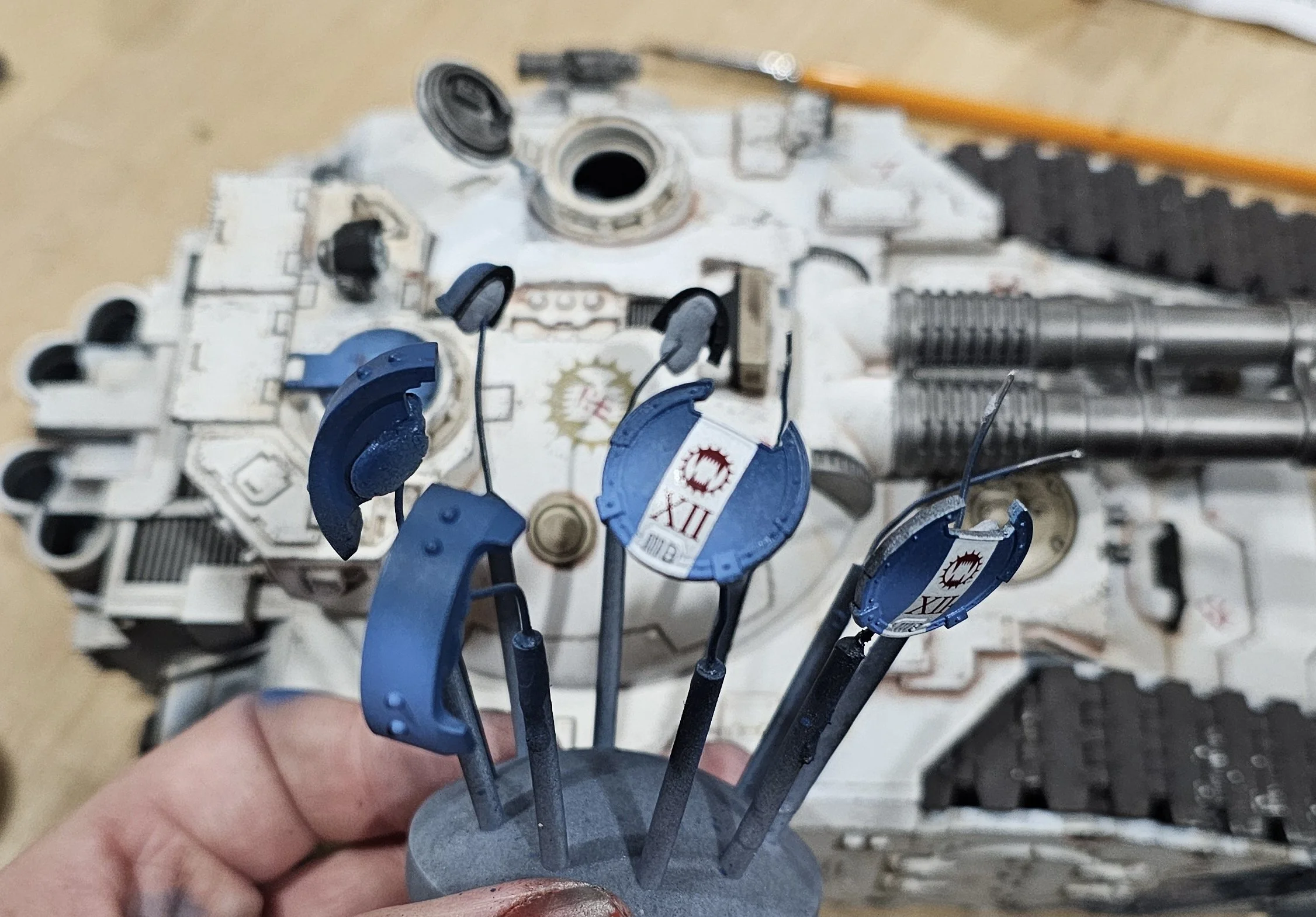 A person holding small painted blue and black model parts for a sci-fi spaceship, with an unassembled spaceship model in the background.