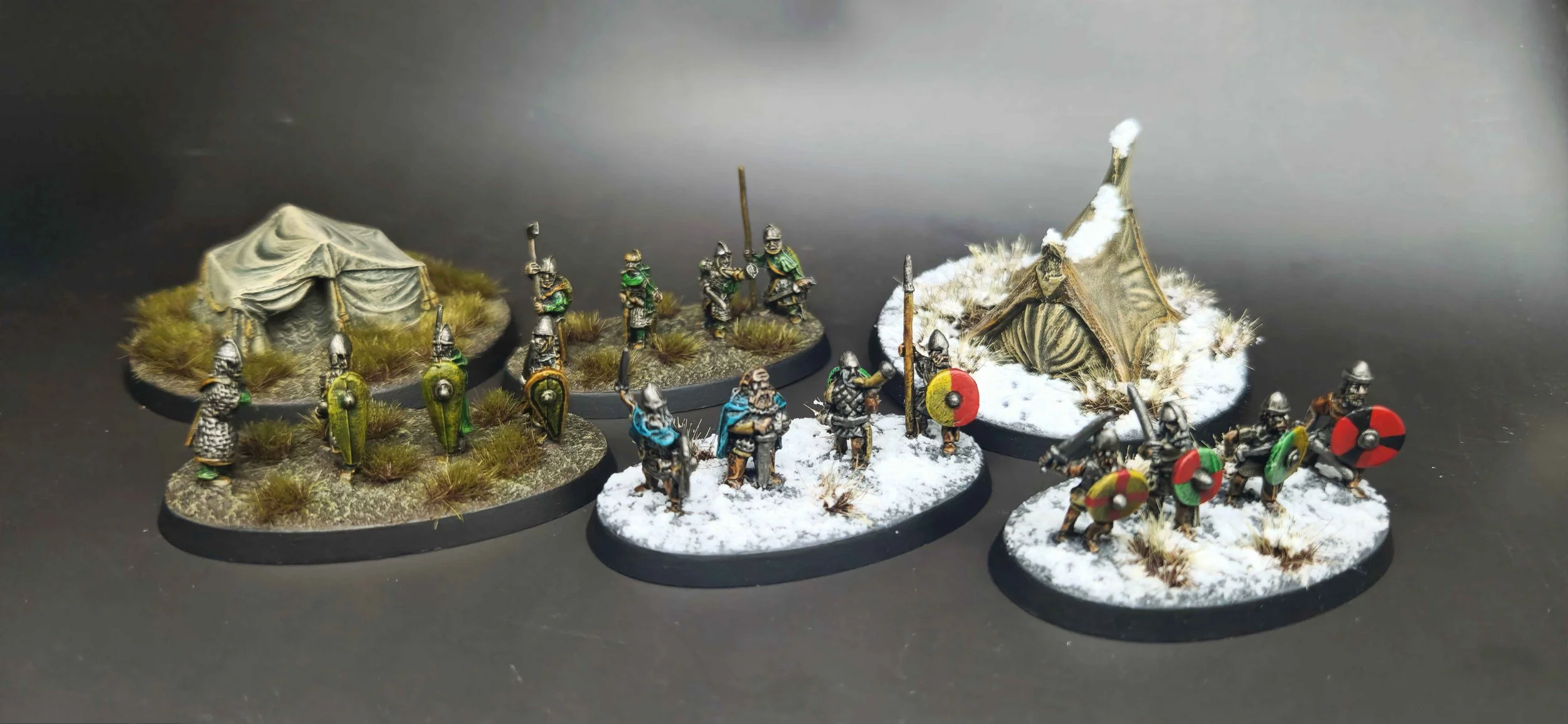 Miniature medieval soldiers and tents on a dark surface, with snow effects on some bases, depicting a miniature battlefield scene.