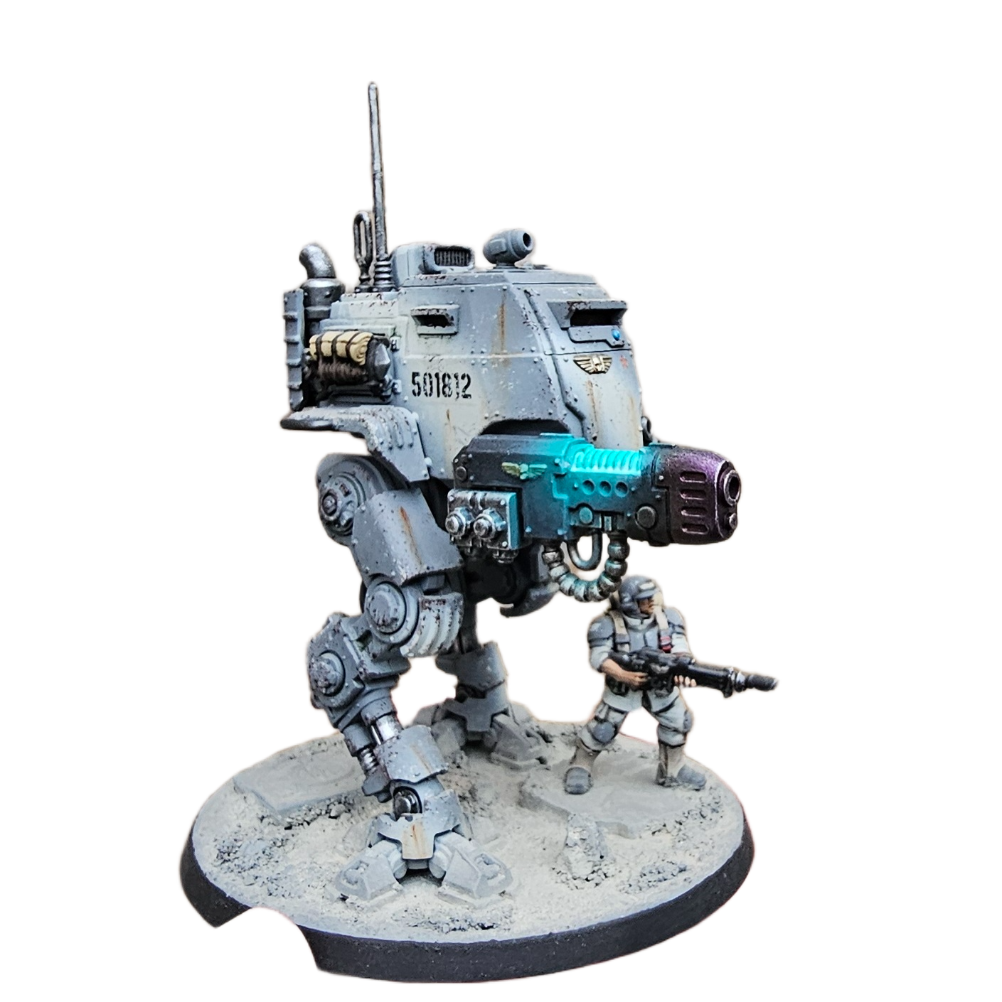 Miniature model of a futuristic exo-mech combat robot with a soldier figure, on a circular sandy base.
