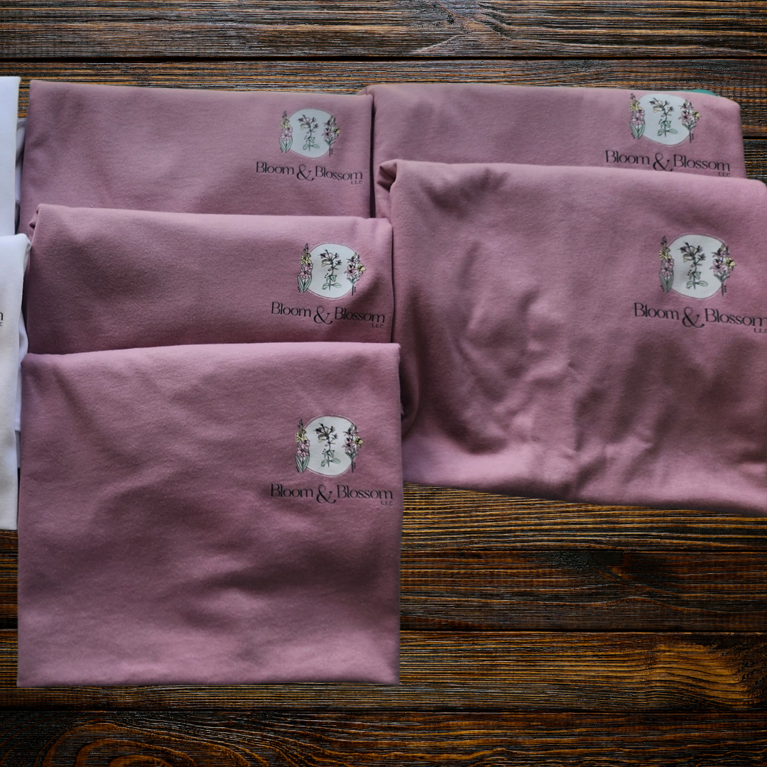 Paños de color rosa con el logotipo de Bloom & Blossom, colocados sobre una mesa de madera marcadamente envejecida.