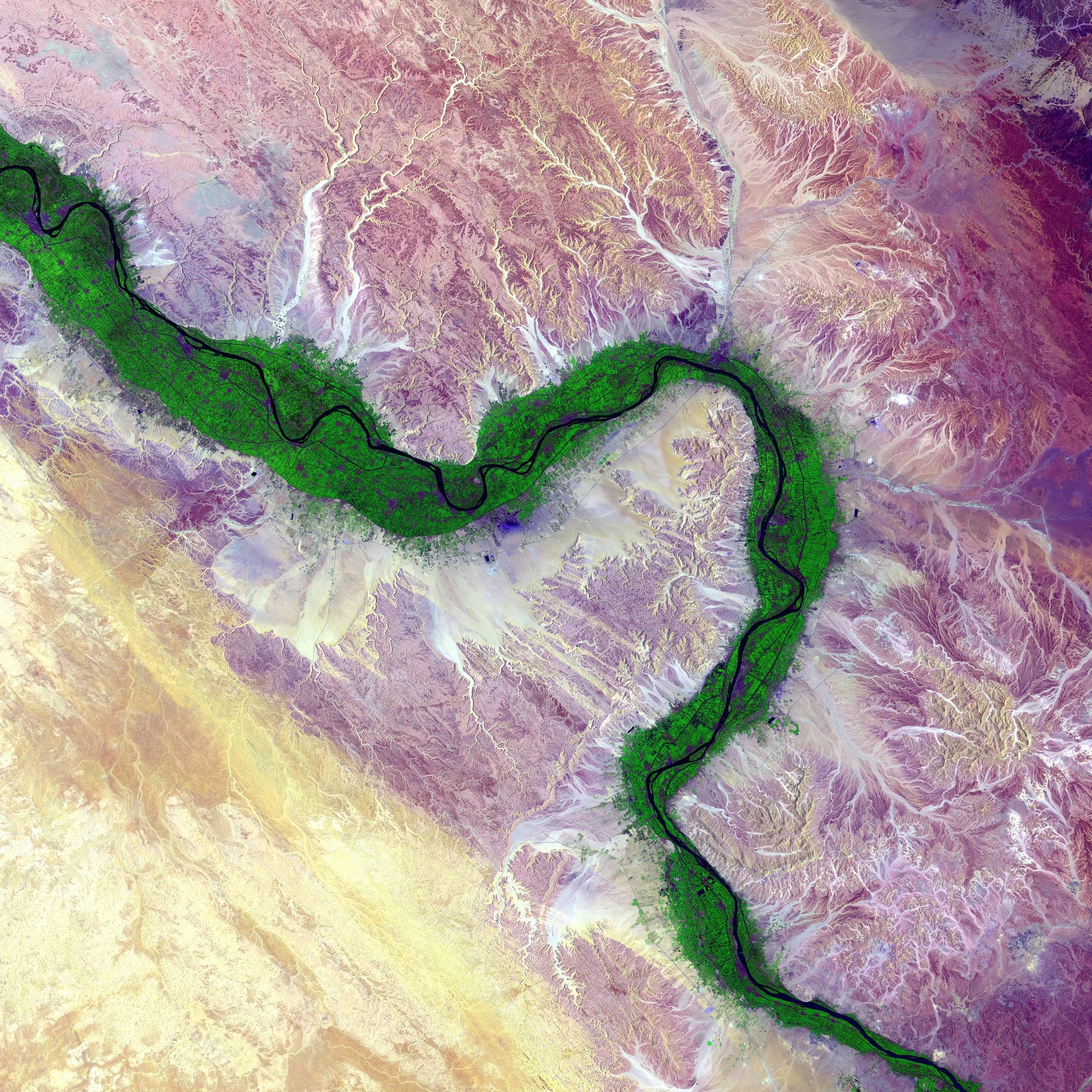 Colorful satellite image of a river winding through a landscape with valleys, mountain ranges, and various terrain types in shades of purple, yellow, and green.