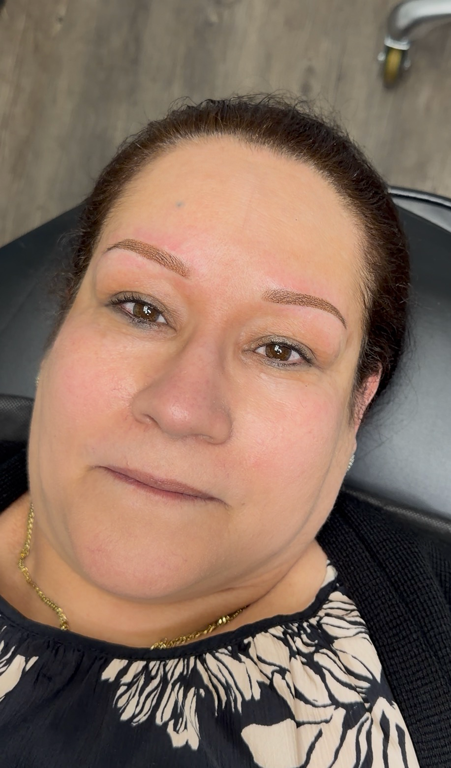 A woman with dark brown hair lying on a black chair, with a wooden floor and a cart wheel visible in the background.